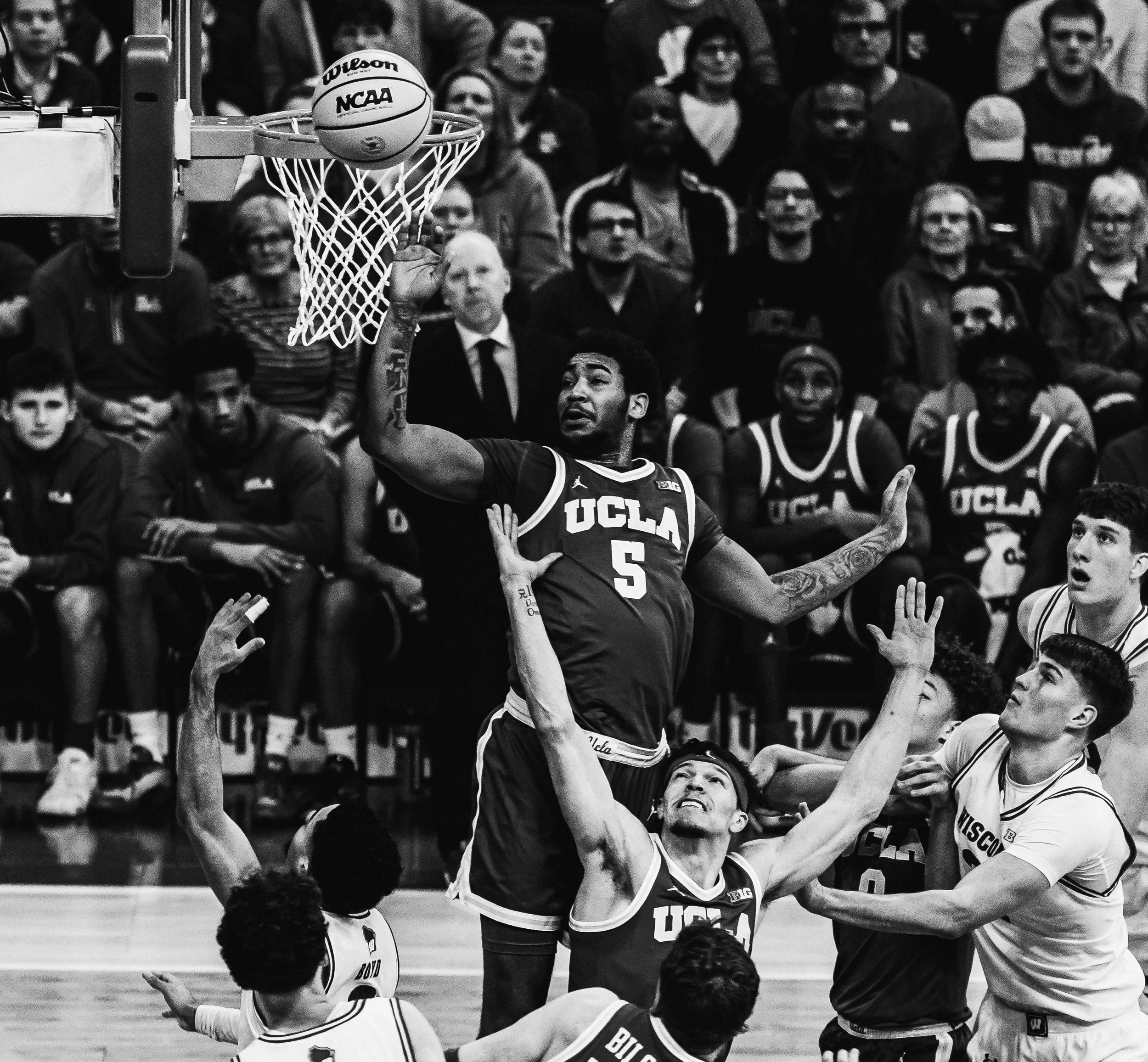 Black and white photo of a basketball game with a player from UCLA attempting a shot towards the hoop, surrounded by teammates and opponents. The crowd in the background watches intently.