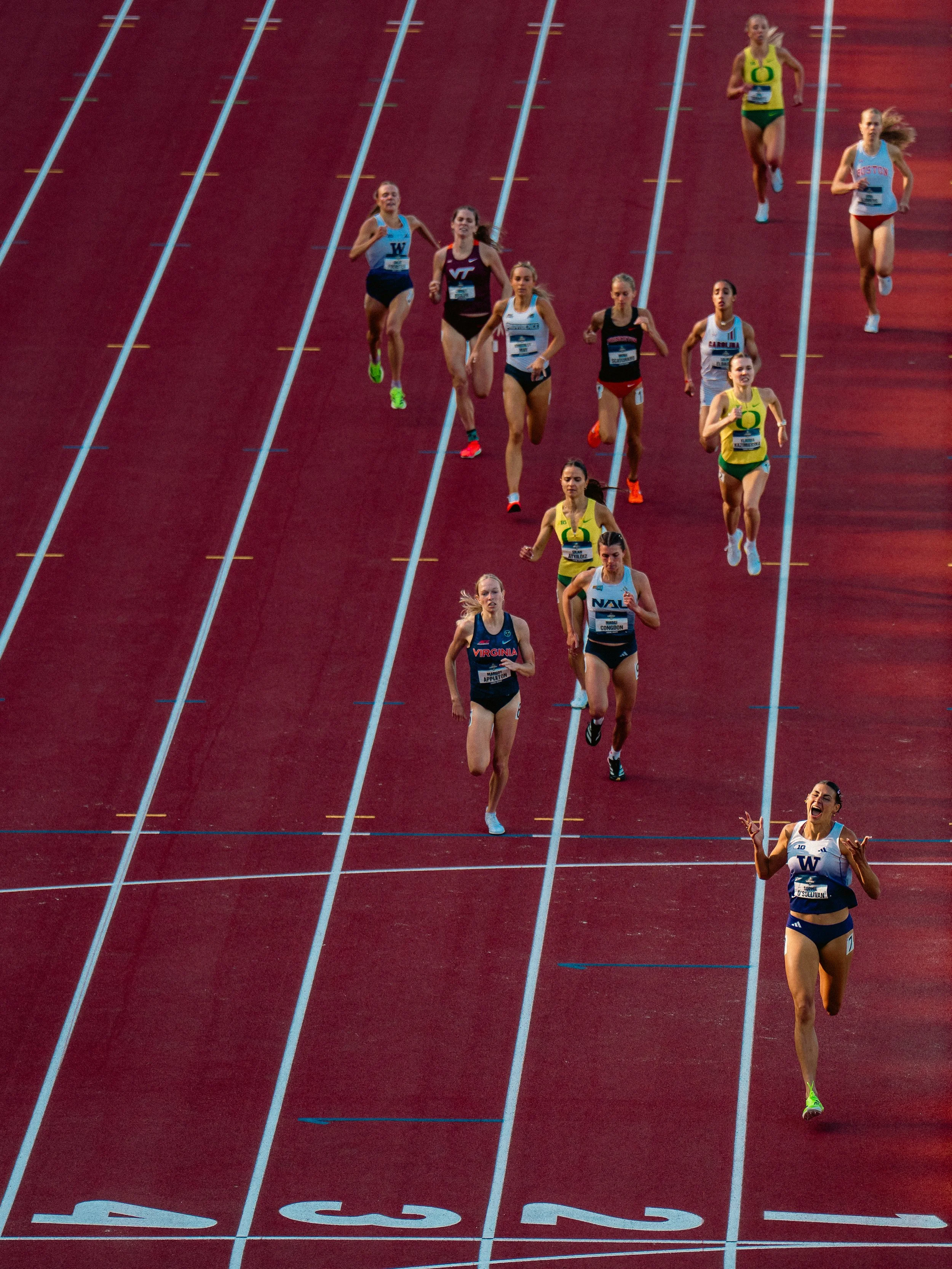 Female athletes running on a red track with white lane markings during a race.