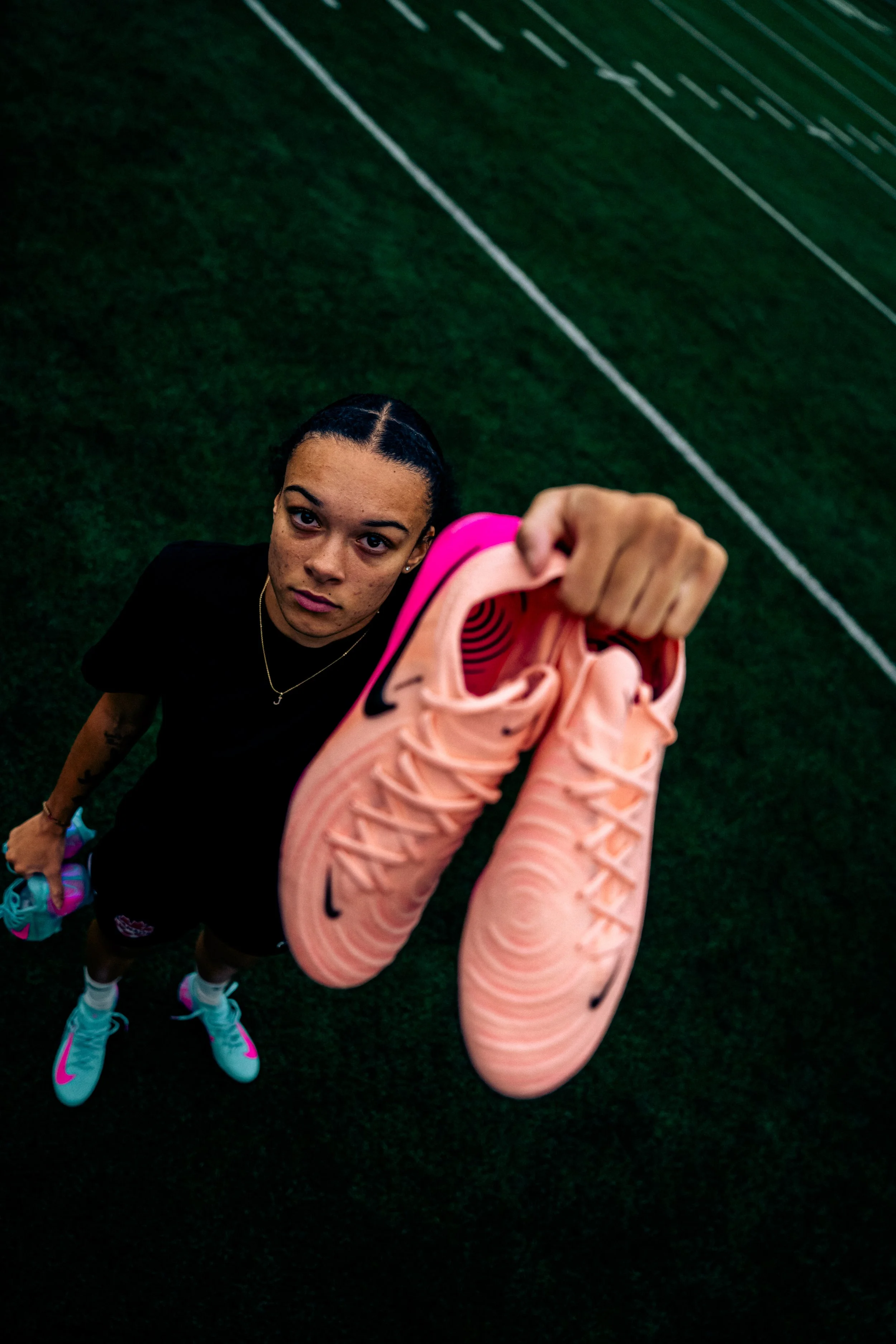 Sportswoman standing on a field, holding a pink athletic shoe with Nike logo, looking up at the camera.