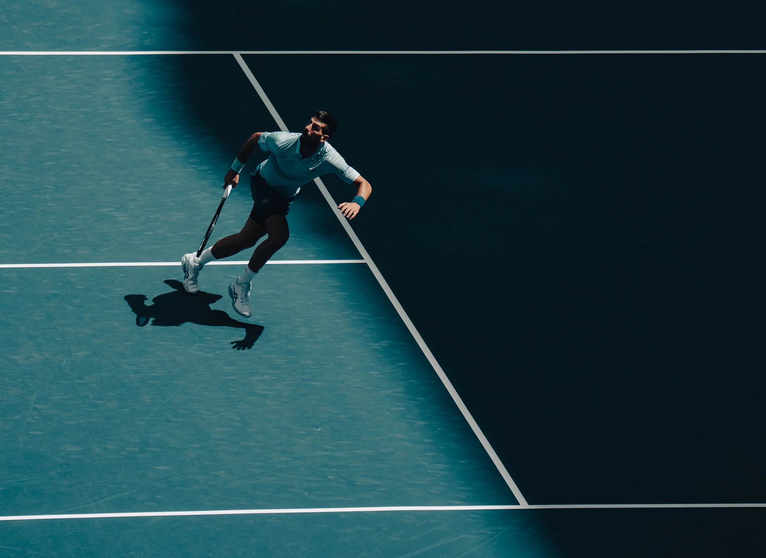 A male tennis player walking on a blue tennis court during a match, holding a tennis racket.