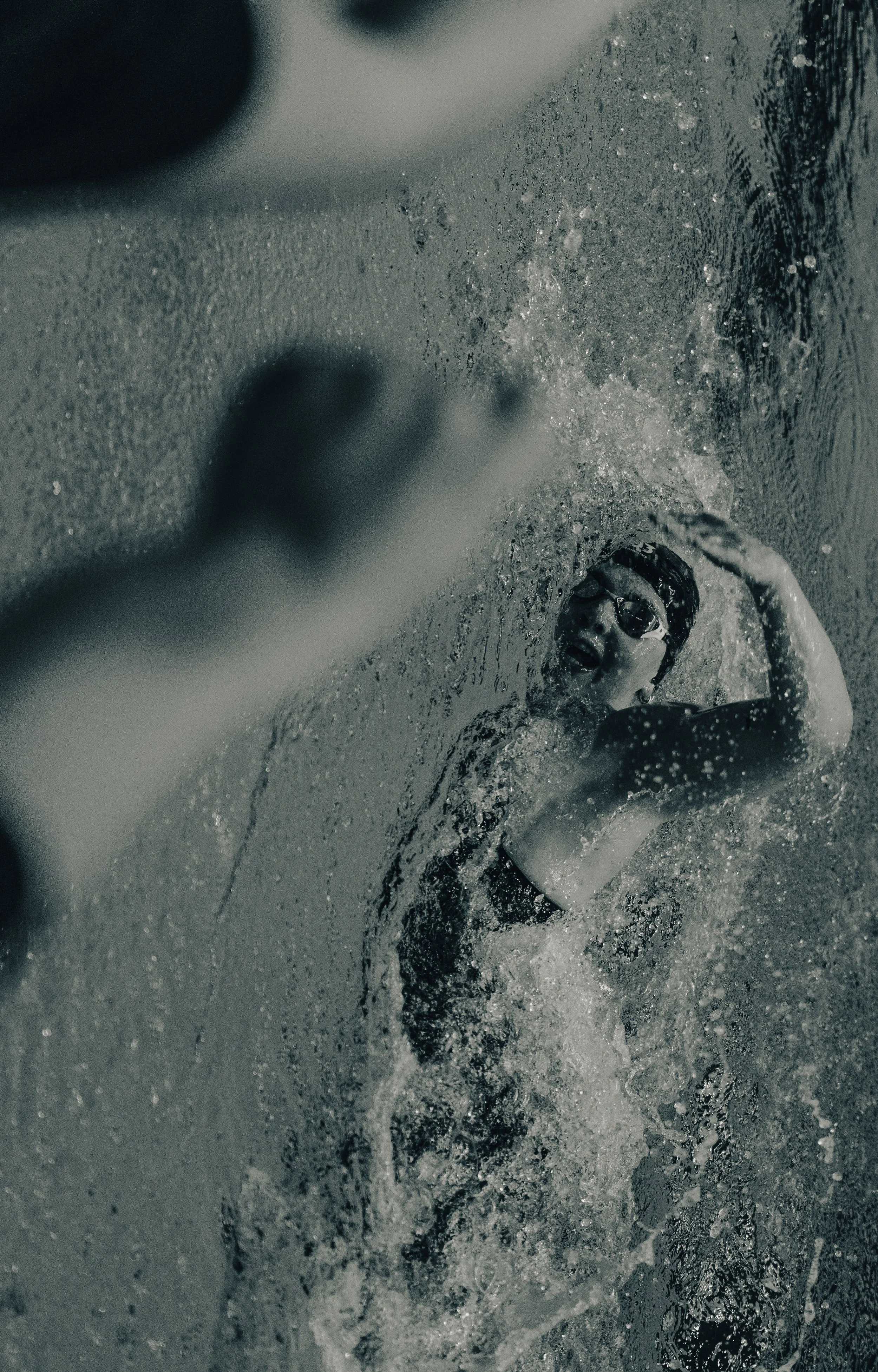 A person swimming underwater with goggles, surrounded by splashing water.