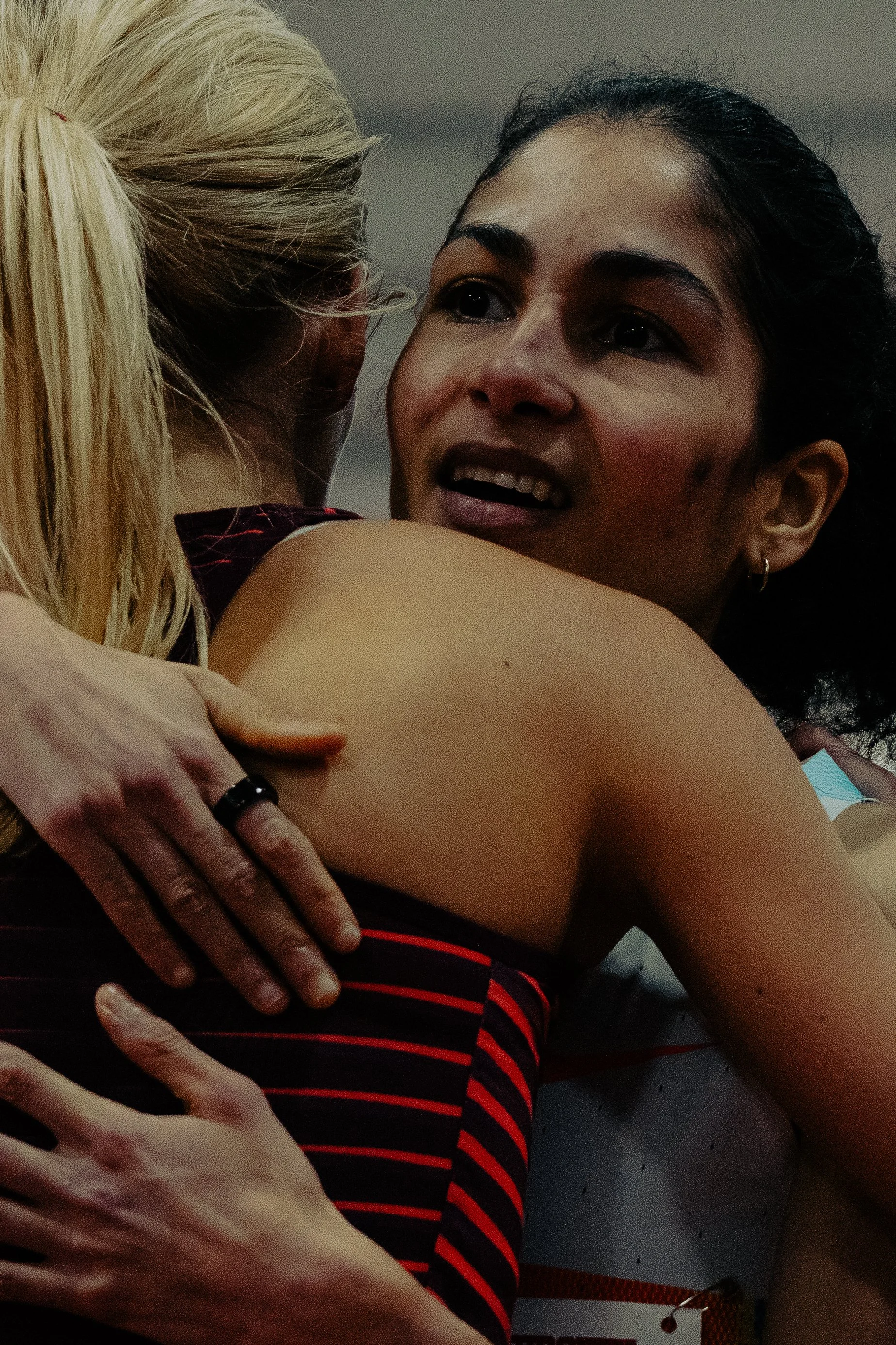 A woman with dark hair and earrings hugging another person with blonde hair and striped clothing.