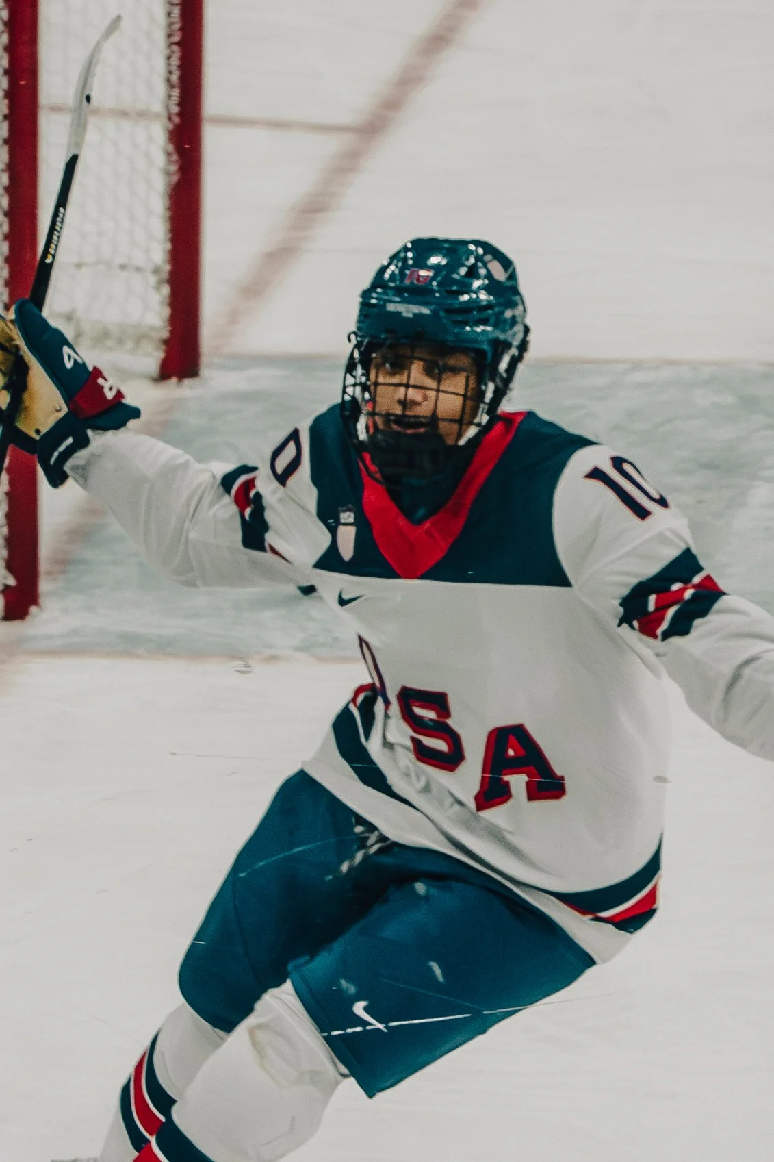 An ice hockey player in a USA jersey celebrating on the ice rink with arms outstretched.