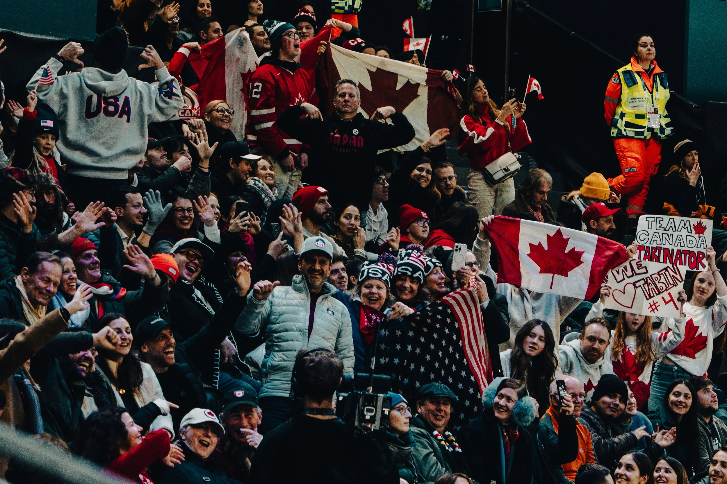 Crowd of enthusiastic sports fans at an event, displaying various flags including Canadian and American flags, and wearing team apparel.