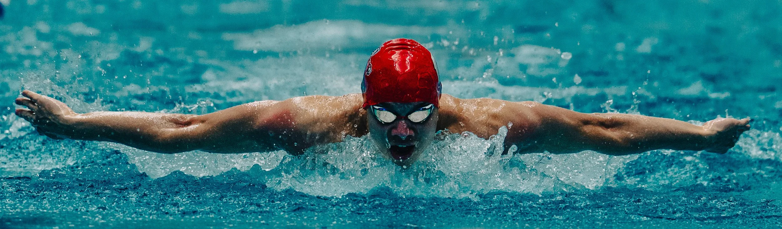 Swimmer in a red cap and goggles performing the butterfly stroke in a swimming pool.