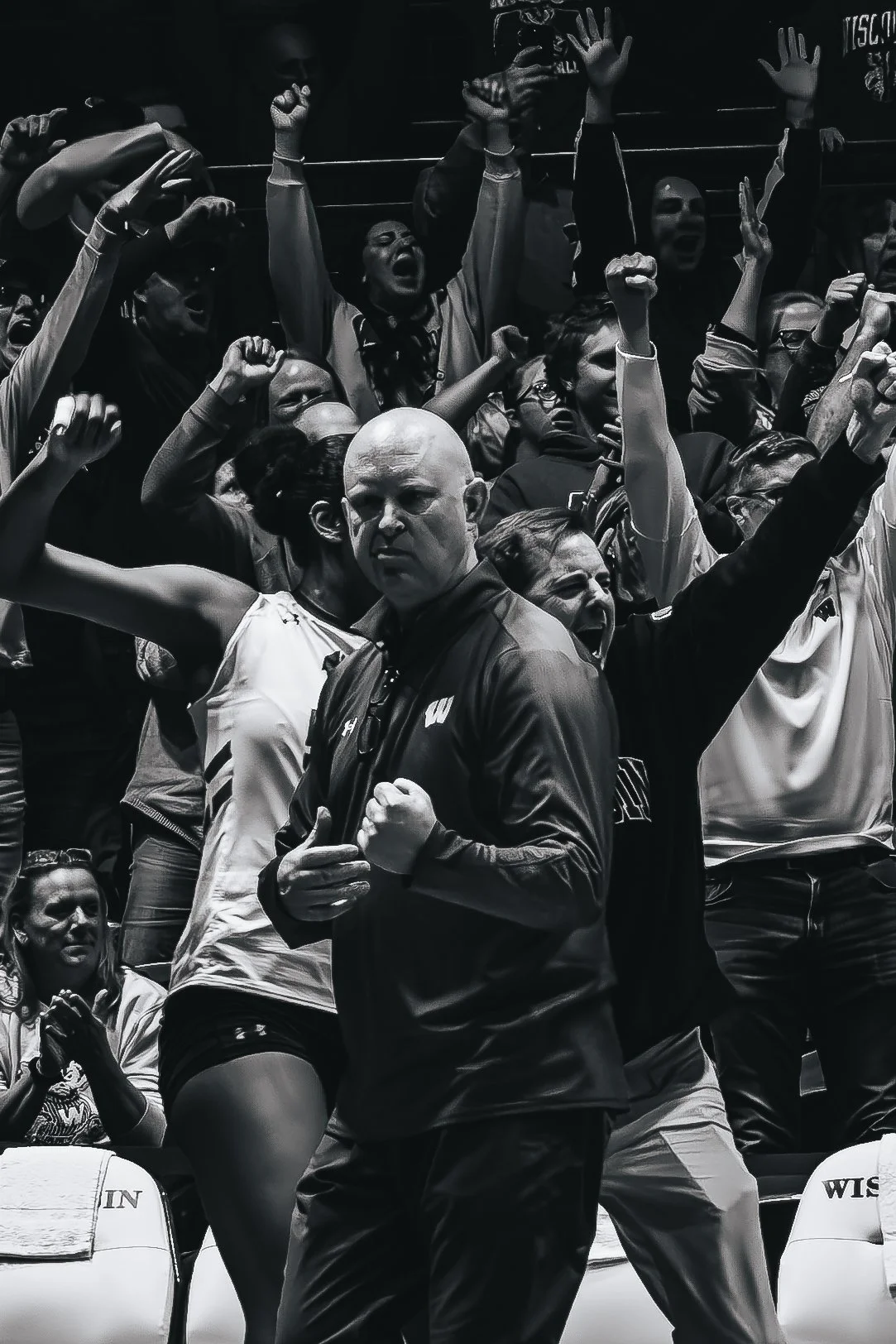 Black and white photo of a crowded sports event, with fans cheering passionately and a coach or official in the foreground.