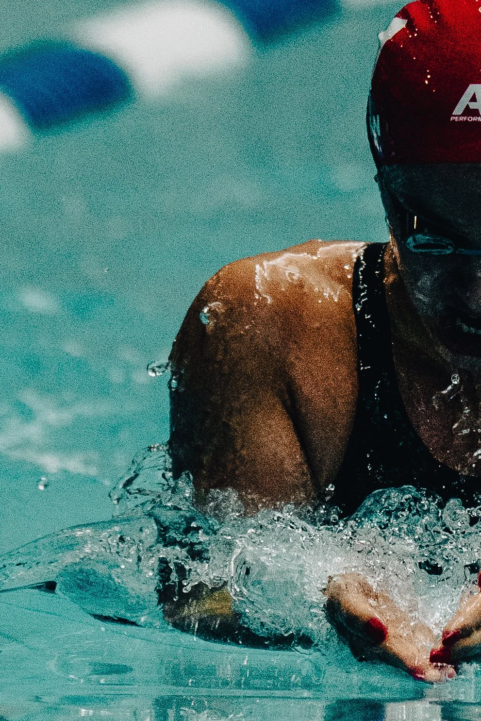 Close-up of a swimmer in a red cap and black swimsuit in the water, with water droplets splashing around.
