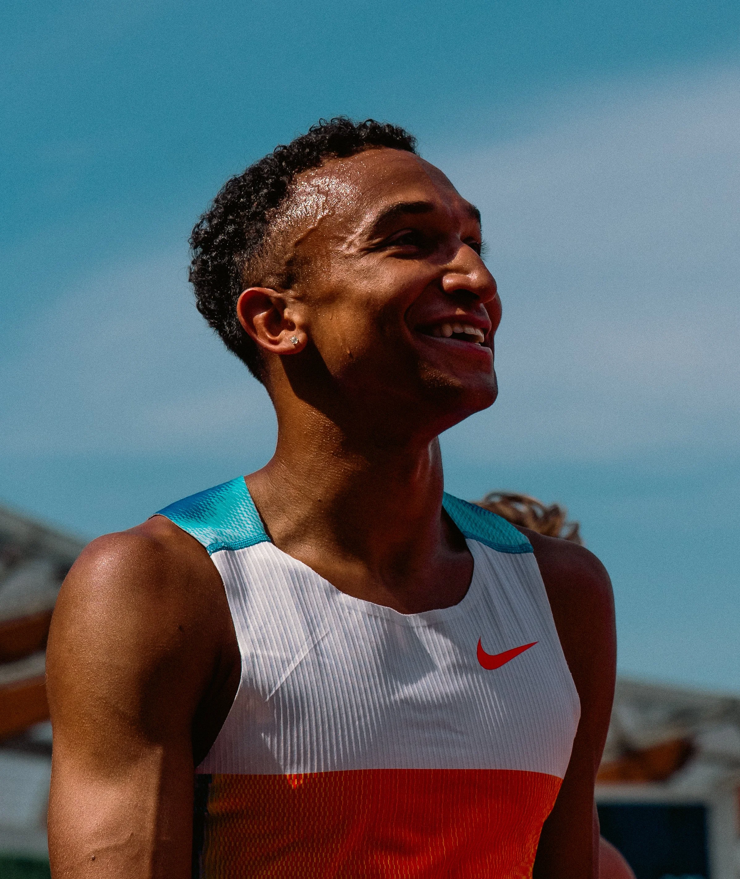 A woman wearing a Nike athletic tank top, smiling while outdoor under a blue sky.