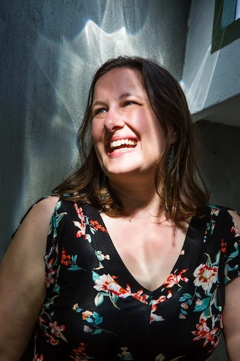 Katrina smiles and looks offer, light reflected on a wall behind her