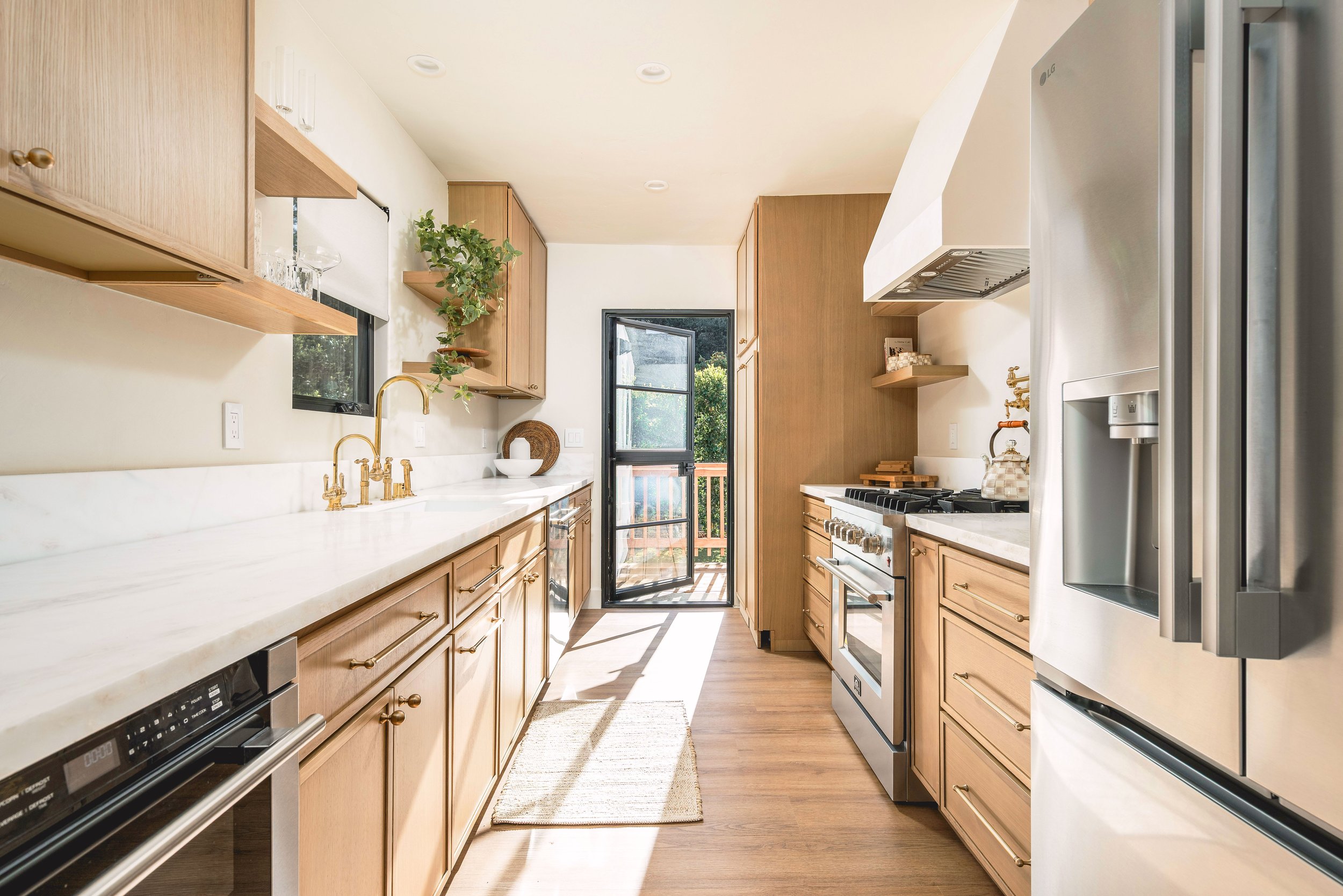 Kitchen with wooden cabinets, white marble countertops, gold fixtures, window, and a door leading outside, with sunlight streaming in.
