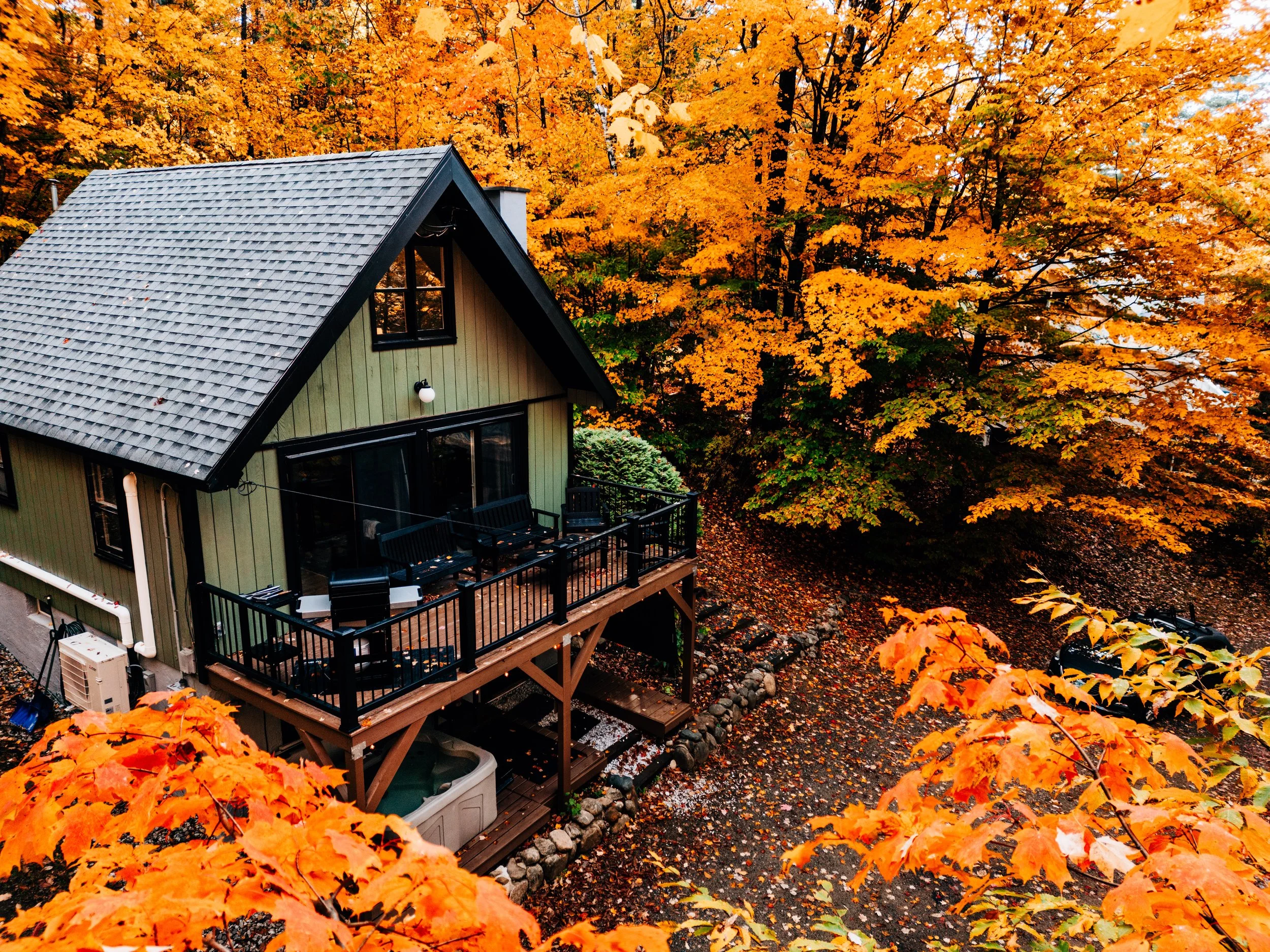 A house with a steep, shingled roof and a balcony, set among trees with vibrant orange and yellow autumn leaves. Vacation Home in White Mountains, NH