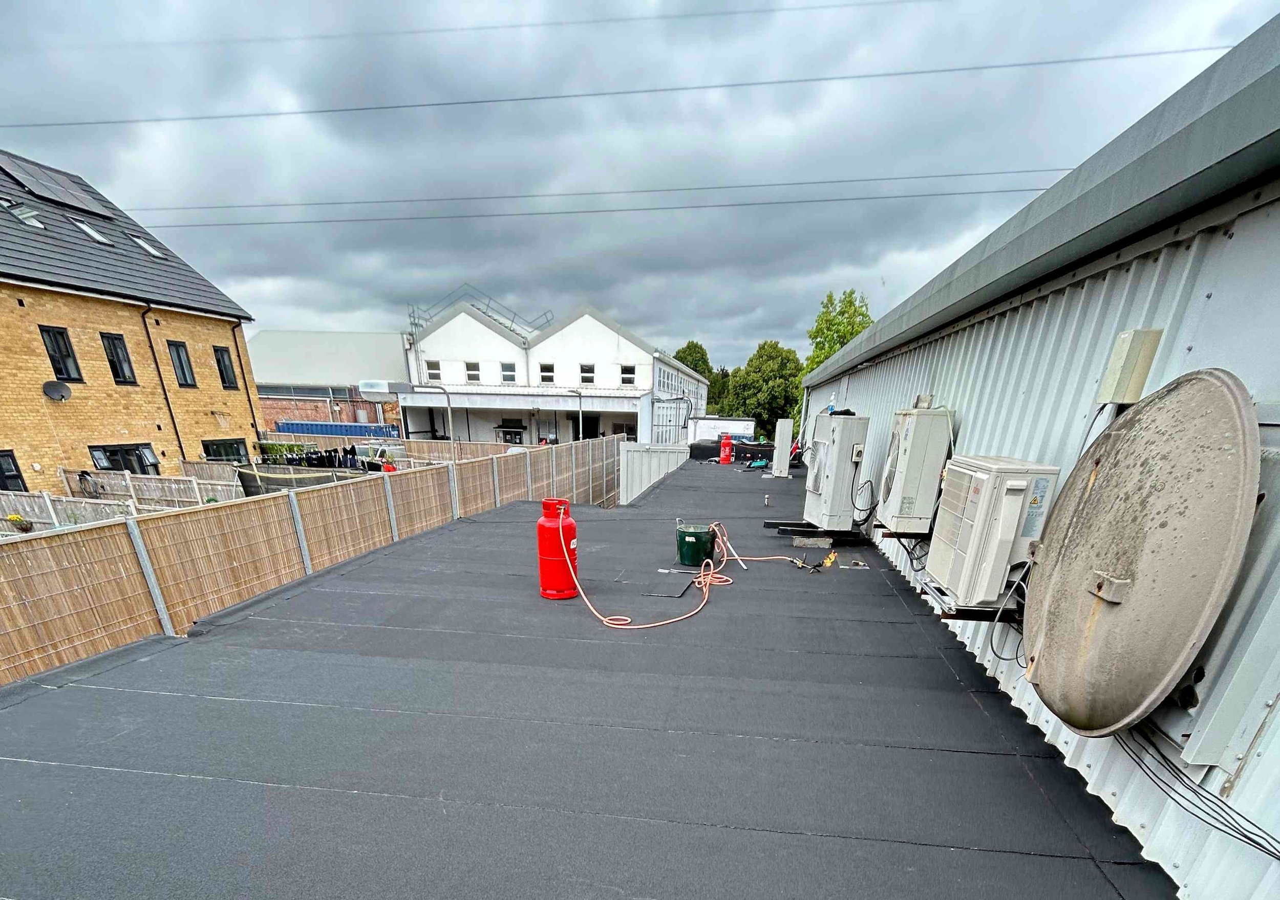 View of a rooftop with solar panels and air conditioning units, a fire extinguisher, and a fenced edge under a cloudy sky.