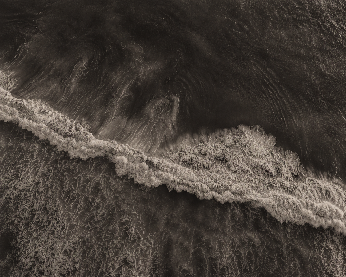 Vista aérea en tonos sepia de olas rompiendo en la playa con espuma rocosa y remolinos en el agua