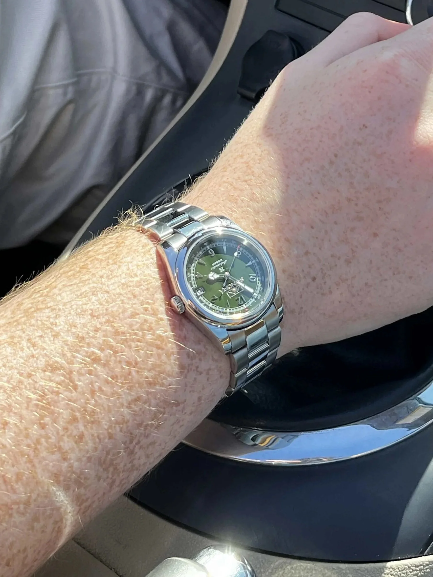 Close-up of a person's wrist wearing a large, silver automatic seiko nh35 watch with a green face, displaying the time, on the person's wrist.