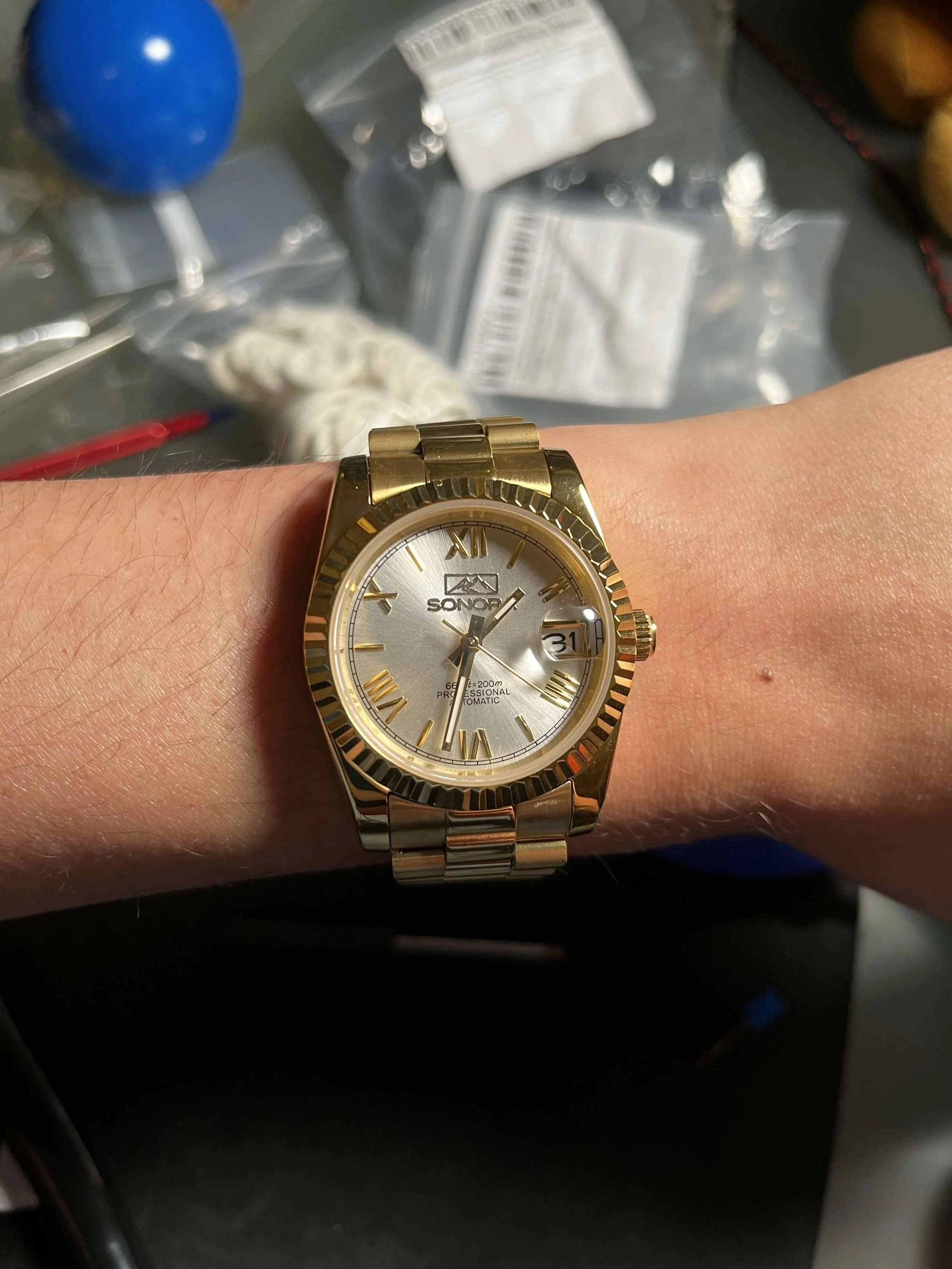 A person's wrist wearing a gold-colored automatic seiko nh35 wristwatch with a fluted datejust bezel with a silver face showing the time, date, and Roman numeral hour markers.