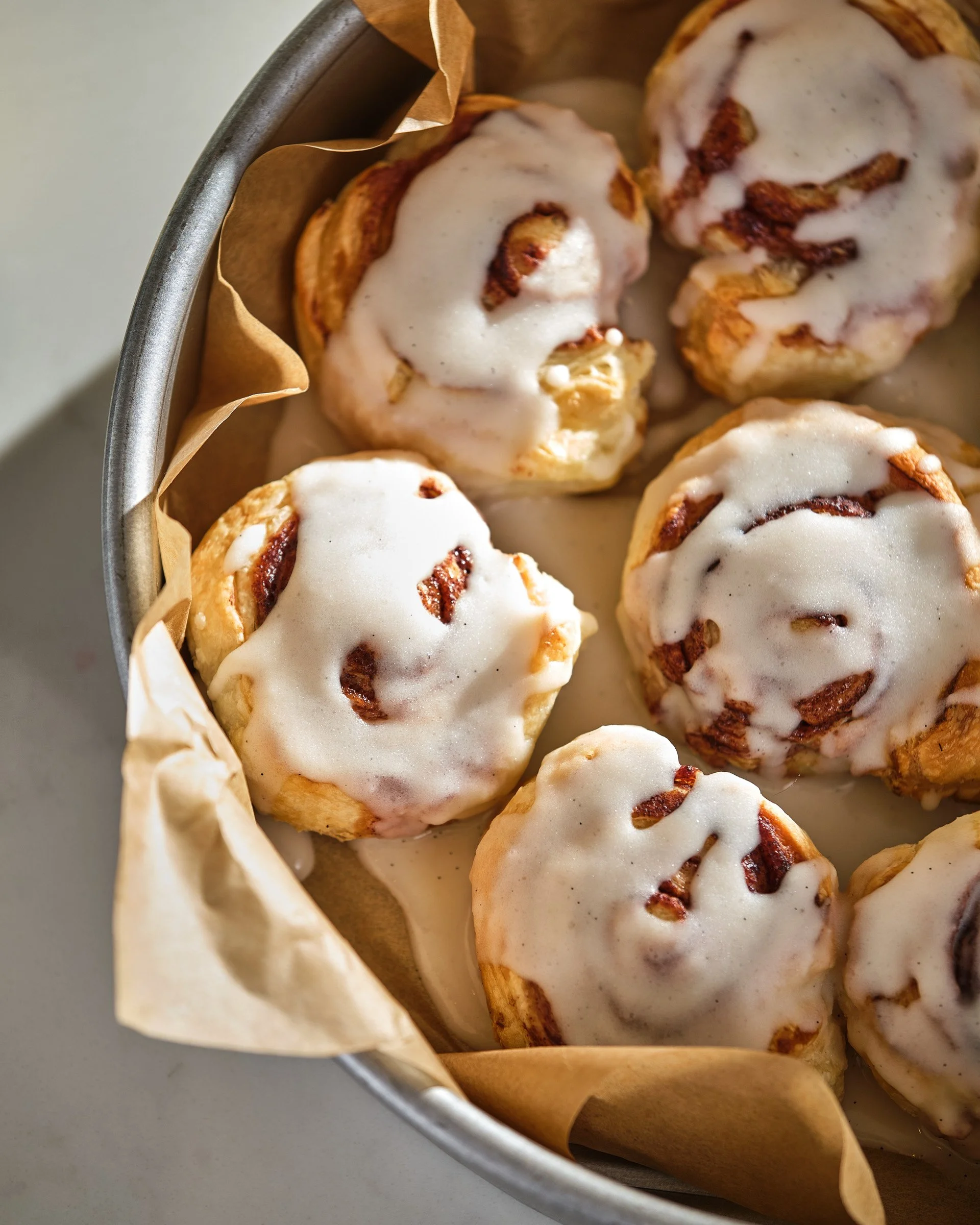 Cinnamon rolls with white icing in a paper-lined metal baking dish.