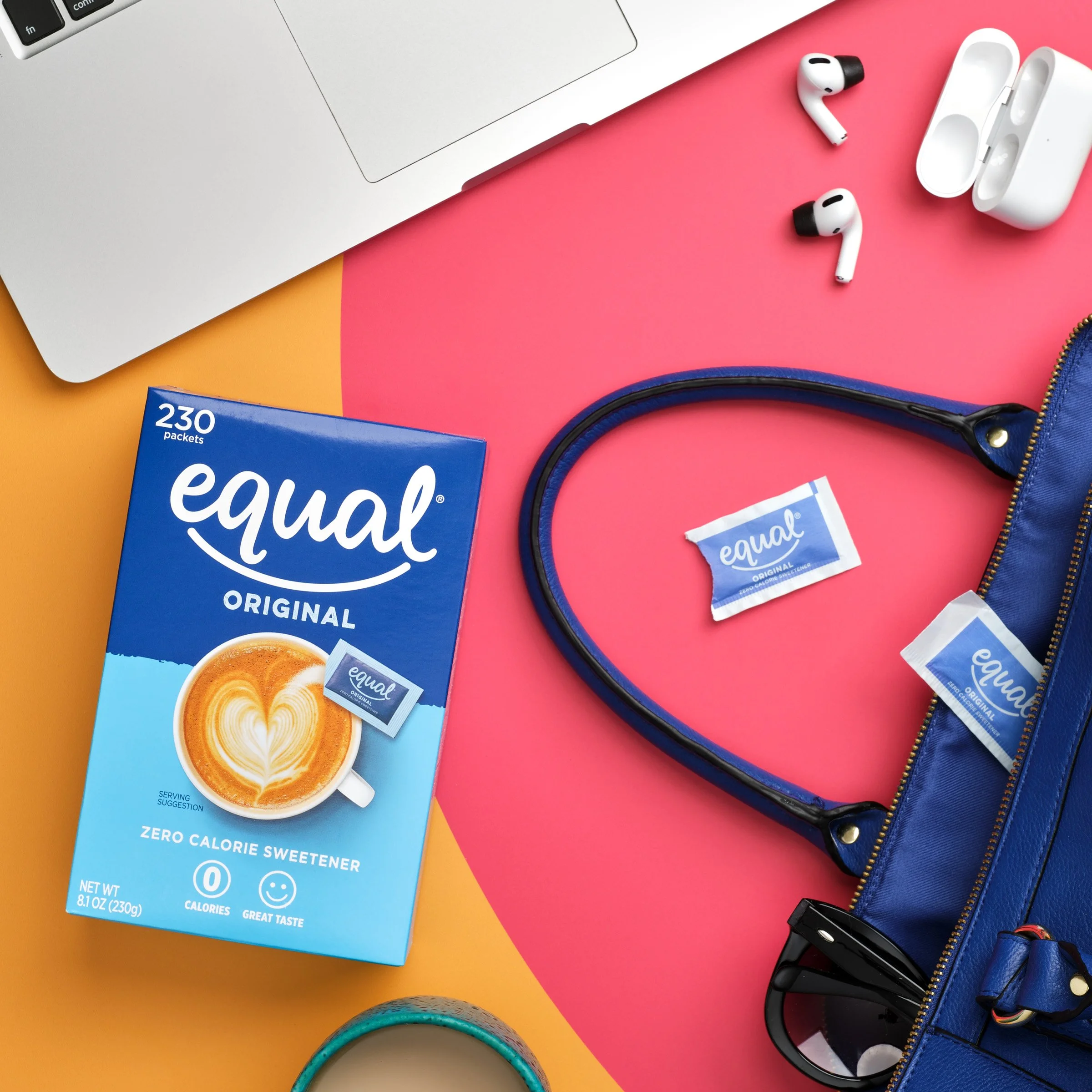 flat lay of a laptop, a box of equal original zero calorie sweetener, a pair of white wireless earbuds with black tips and their case, a blue zippered bag, a packet of tape, and a pair of sunglasses on a colorful background of yellow, pink, and orang