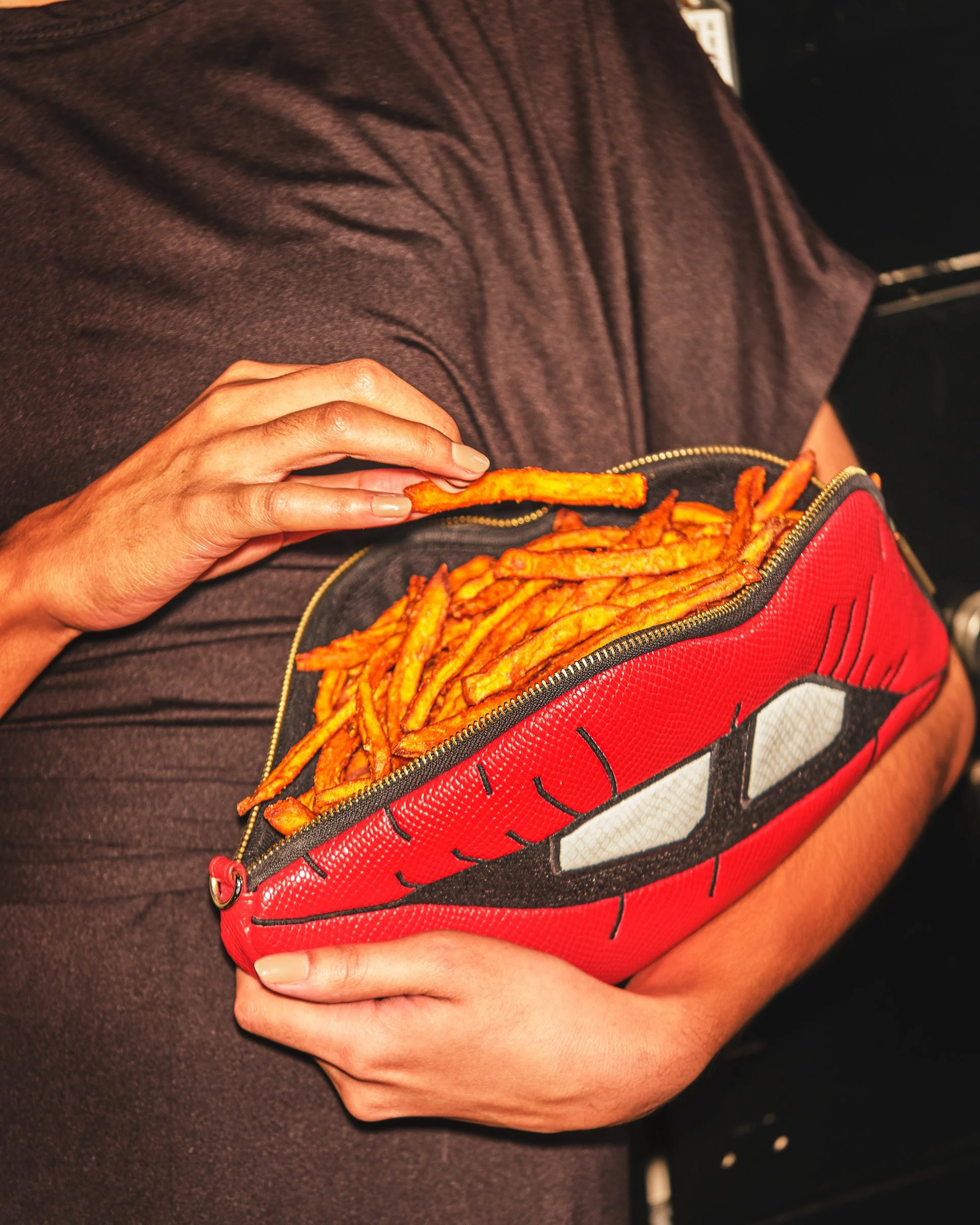 Person holding a red character-themed bag filled with cooked curly fries, sitting on a dark surface.