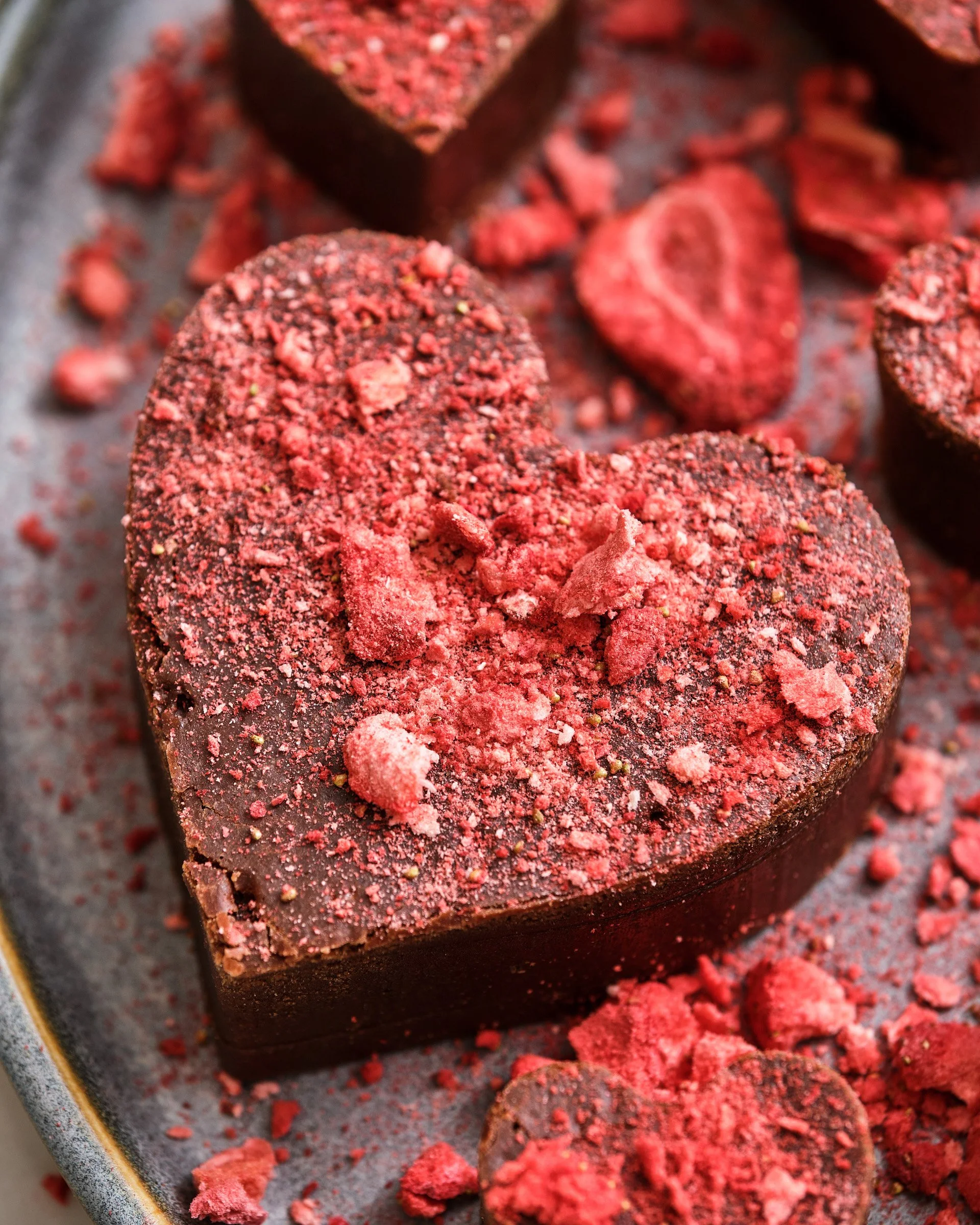 Close-up of a tray of crushed red cookie or cake pieces and whole candy or cake-coated chocolates, with one large chocolate coated piece in the foreground.