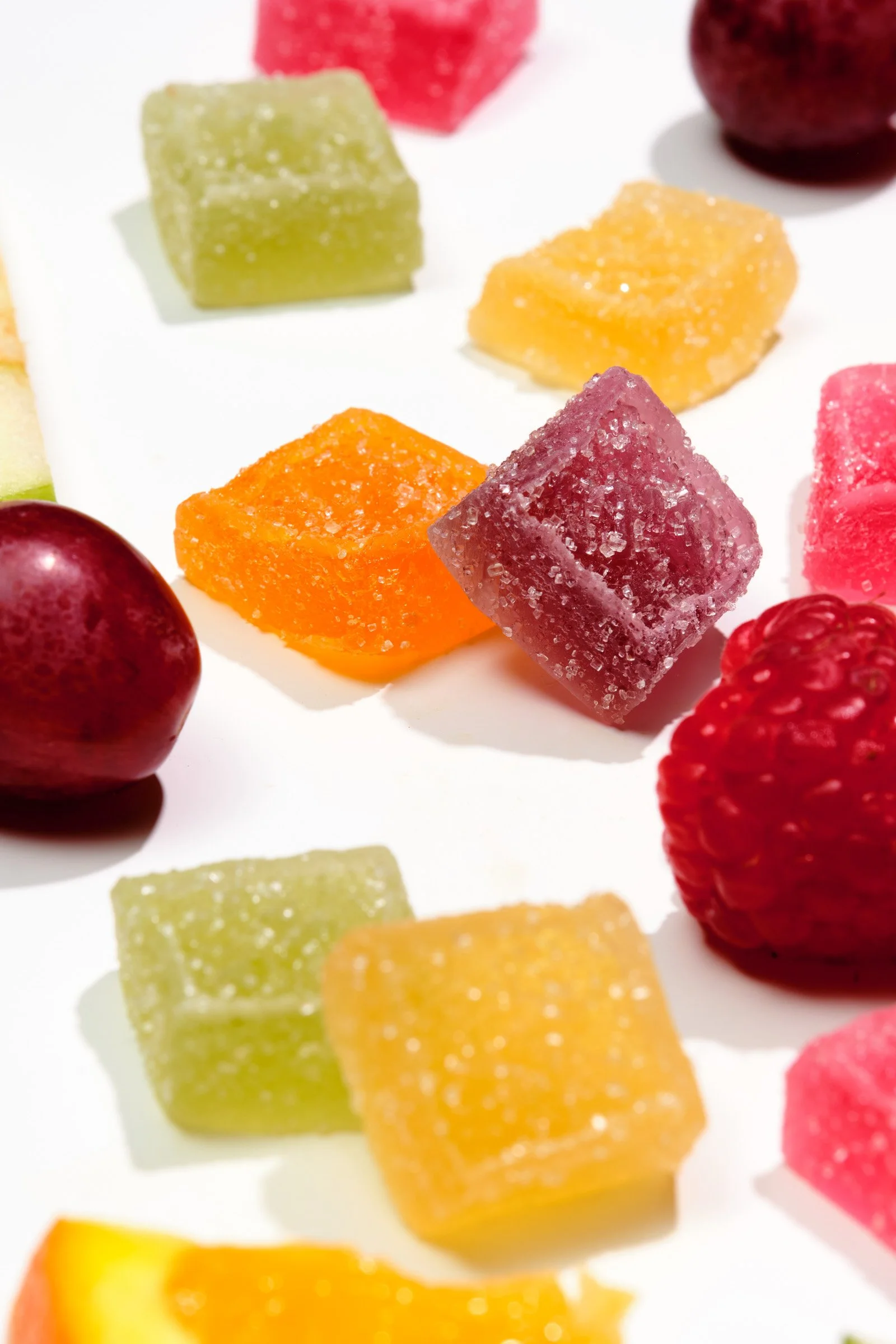 Close-up of assorted fruit-flavored gummy candies on a white surface.