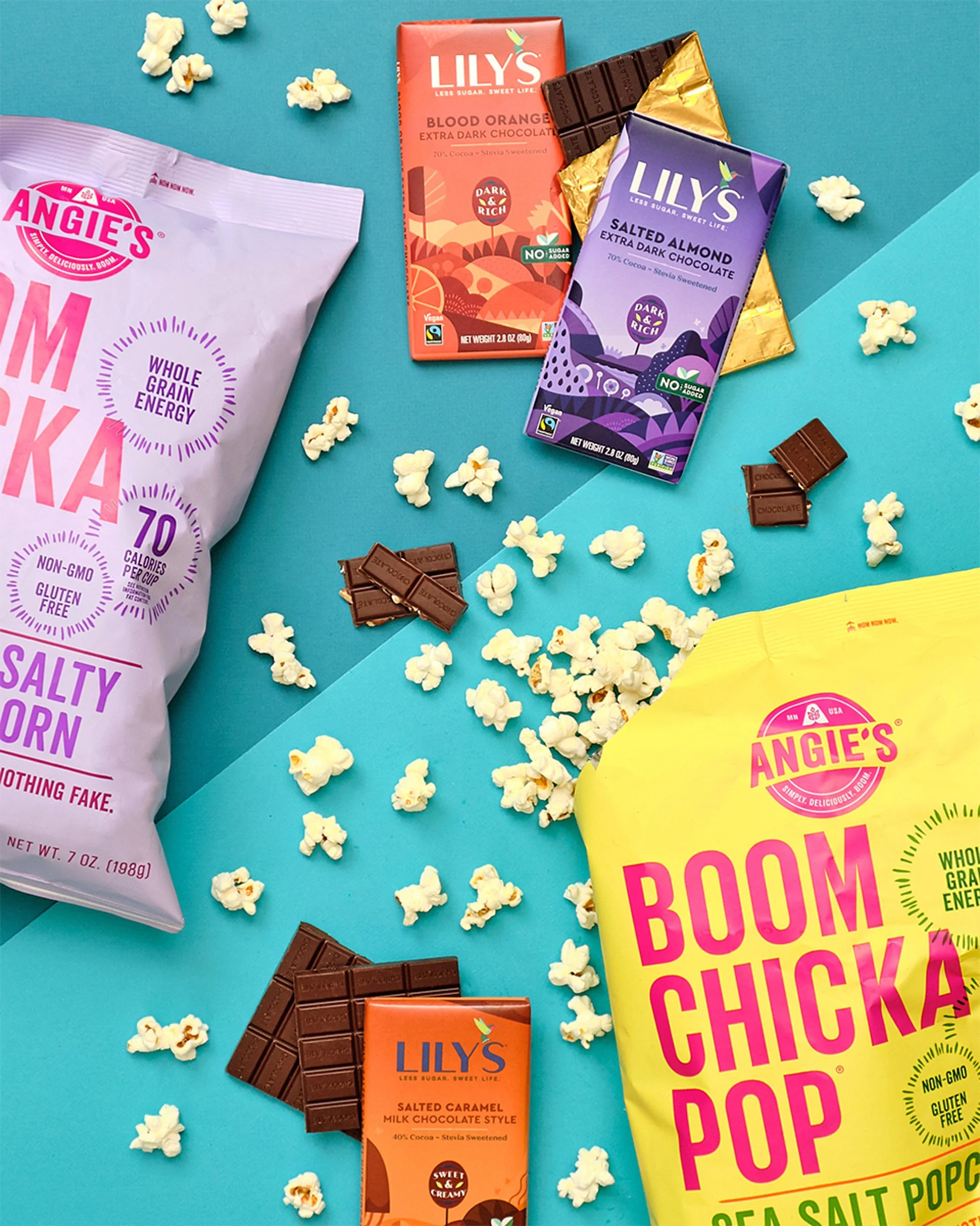 Various flavors of Lily's dark chocolate bars, popcorn scattered around, pieces of broken chocolate, and a yellow bag of Angie’s popcorn on a blue background.