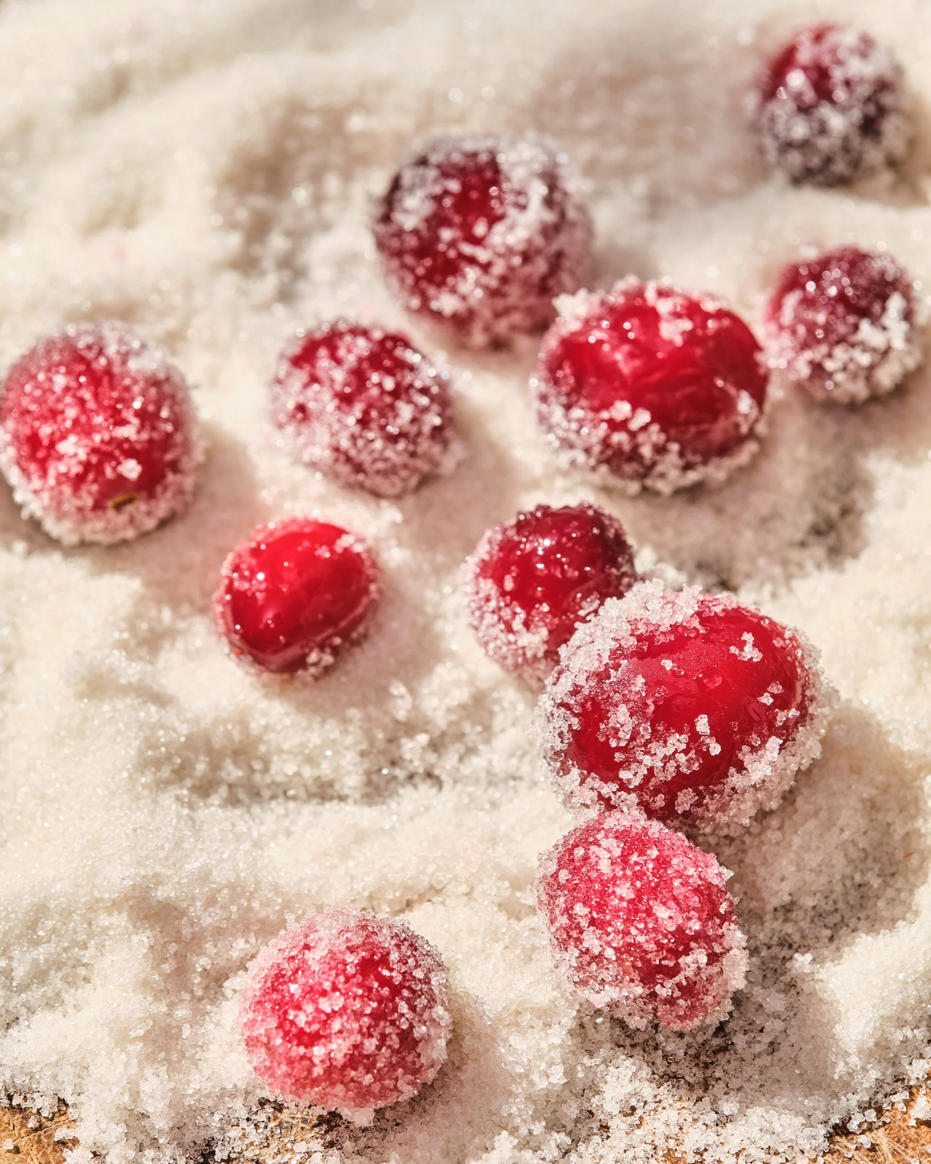 Red raspberries covered in sugar resting on a bed of white sugar.