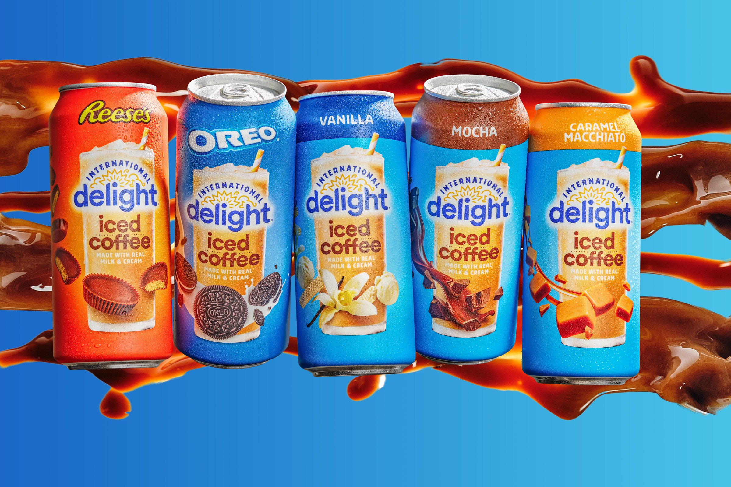 A collection of five flavored International Delight Iced Coffee cans, including Reese's, Oreo, vanilla, mocha, and caramel macchiato, against a blue background with splashes of iced coffee.