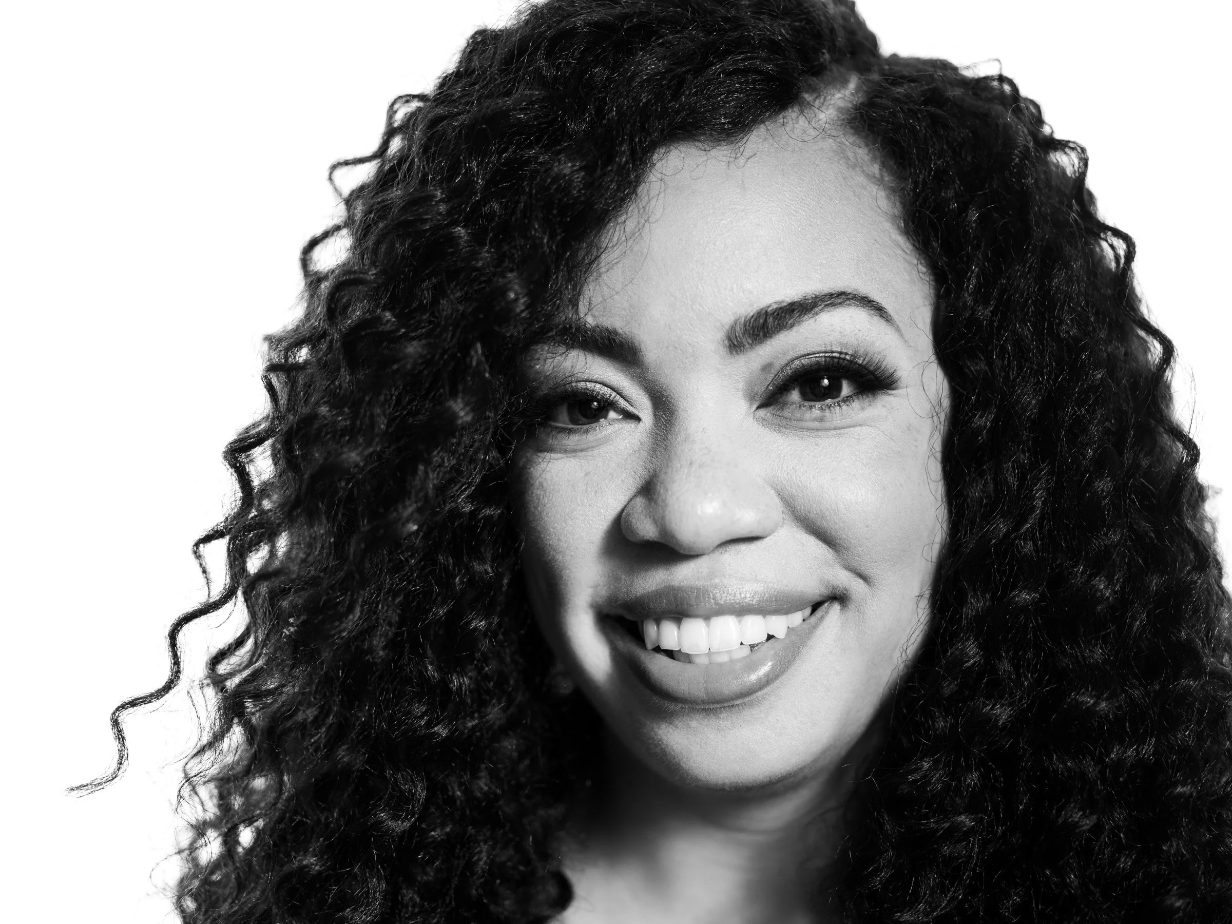 Close-up of a woman with curly hair smiling with visible teeth