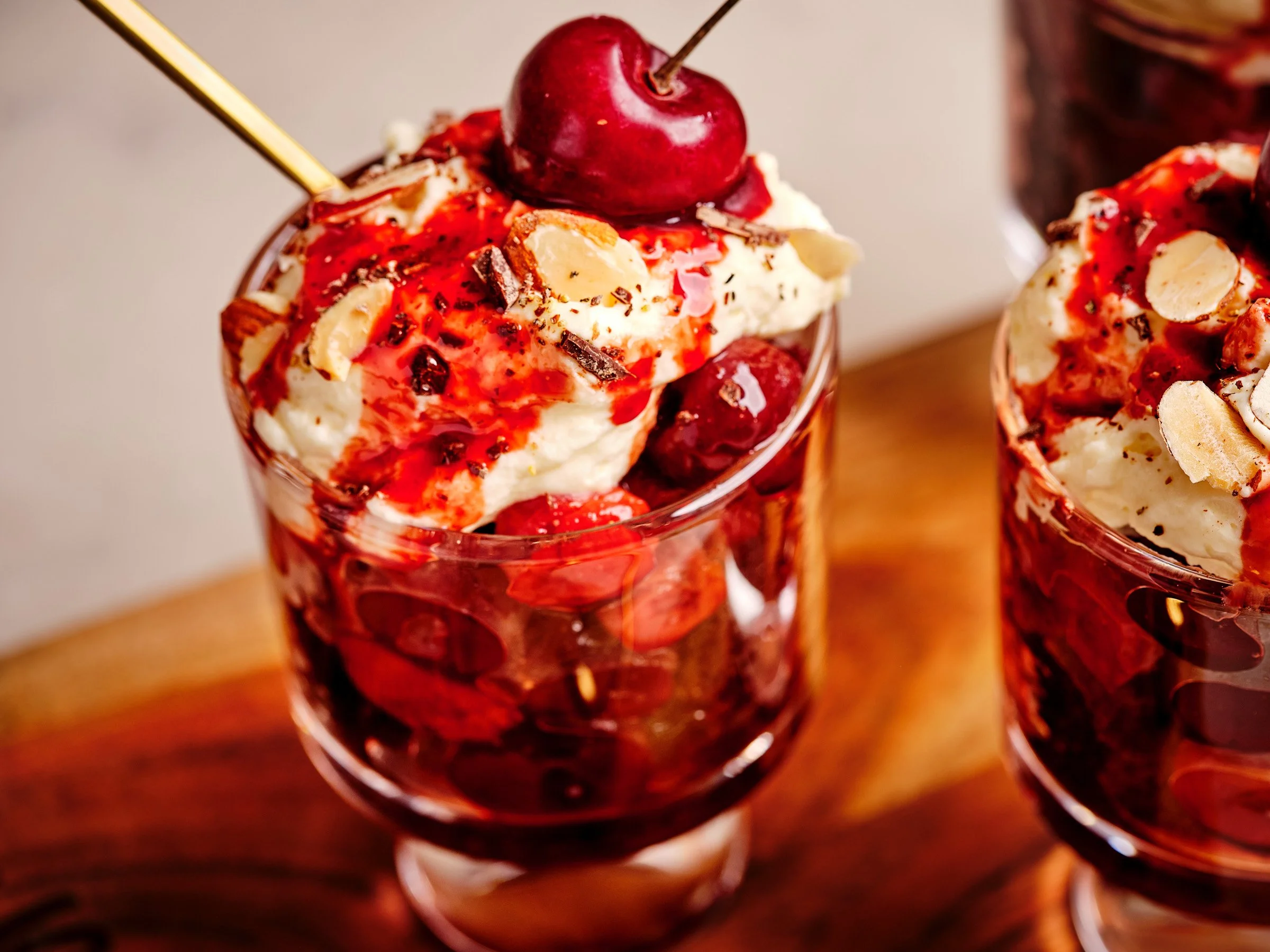 A dessert glass filled with ice cream topped with cherries, whipped cream, chocolate shavings, and cherry syrup.
