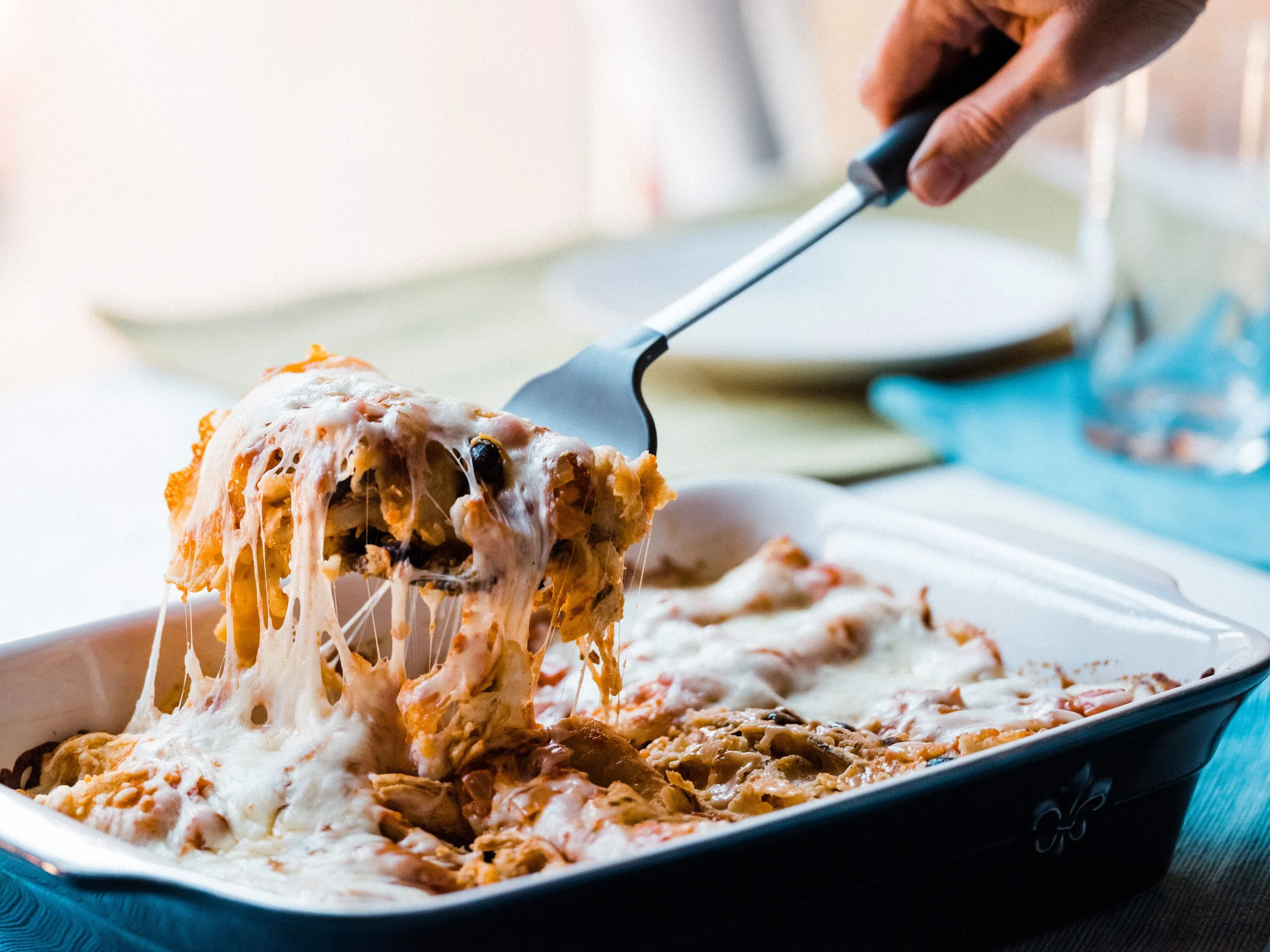 A person serving a enchiladas with melted cheese from a black serving tray.