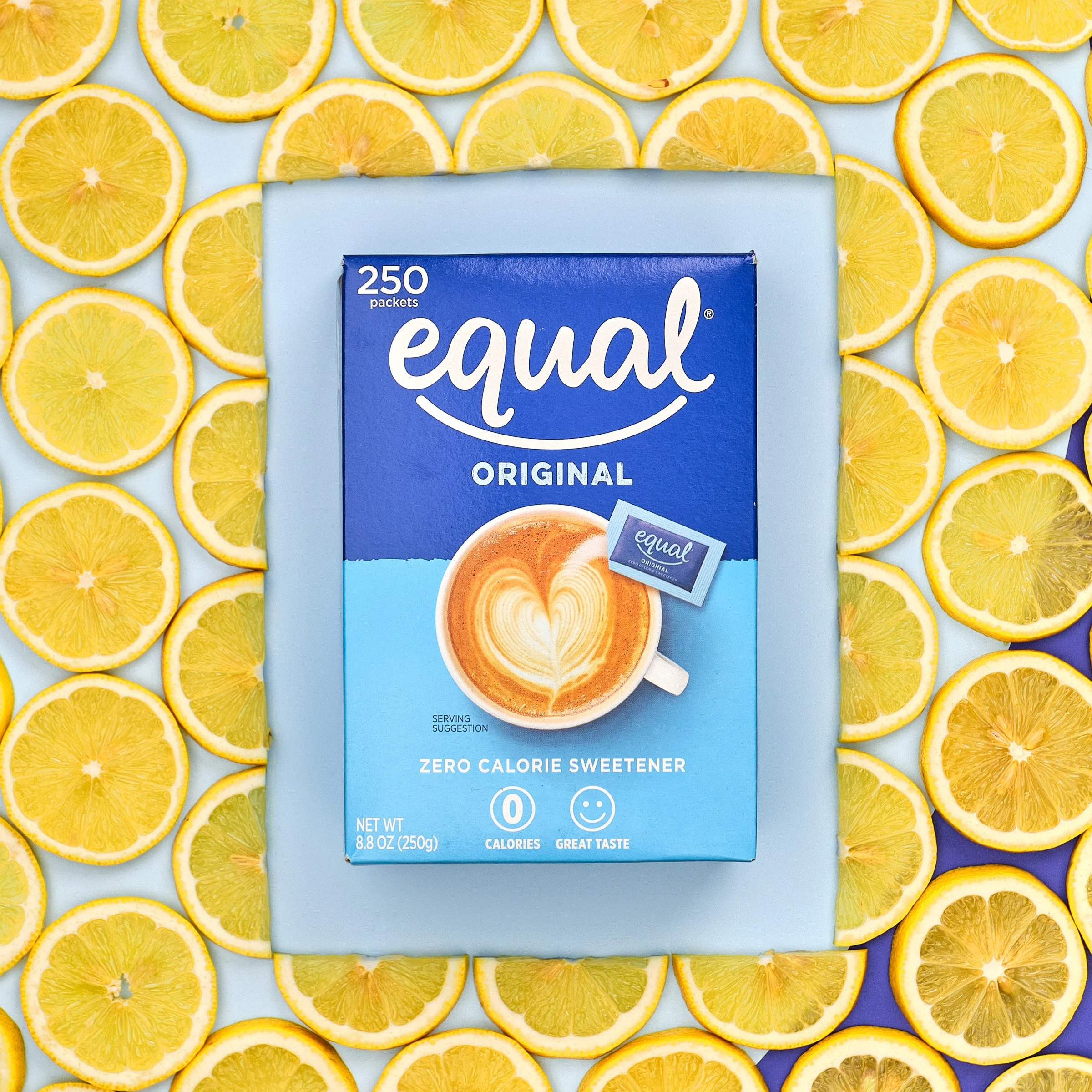 A box of equal original zero calorie sweetener surrounded by lemon slices on a light blue background.