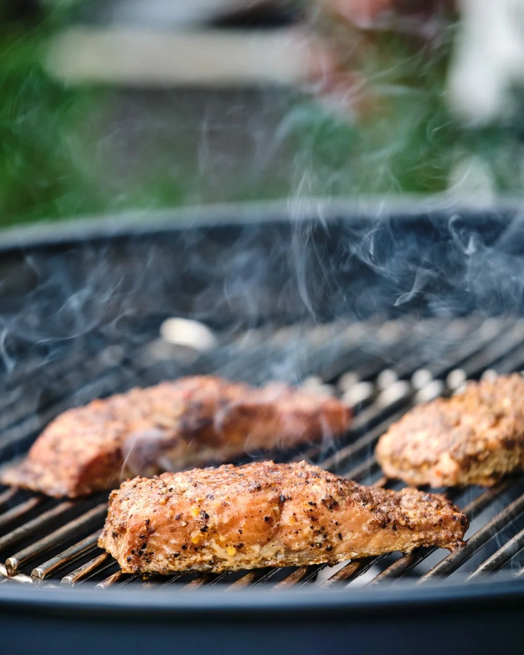 Meat grilling on a barbecue grill with smoke rising.