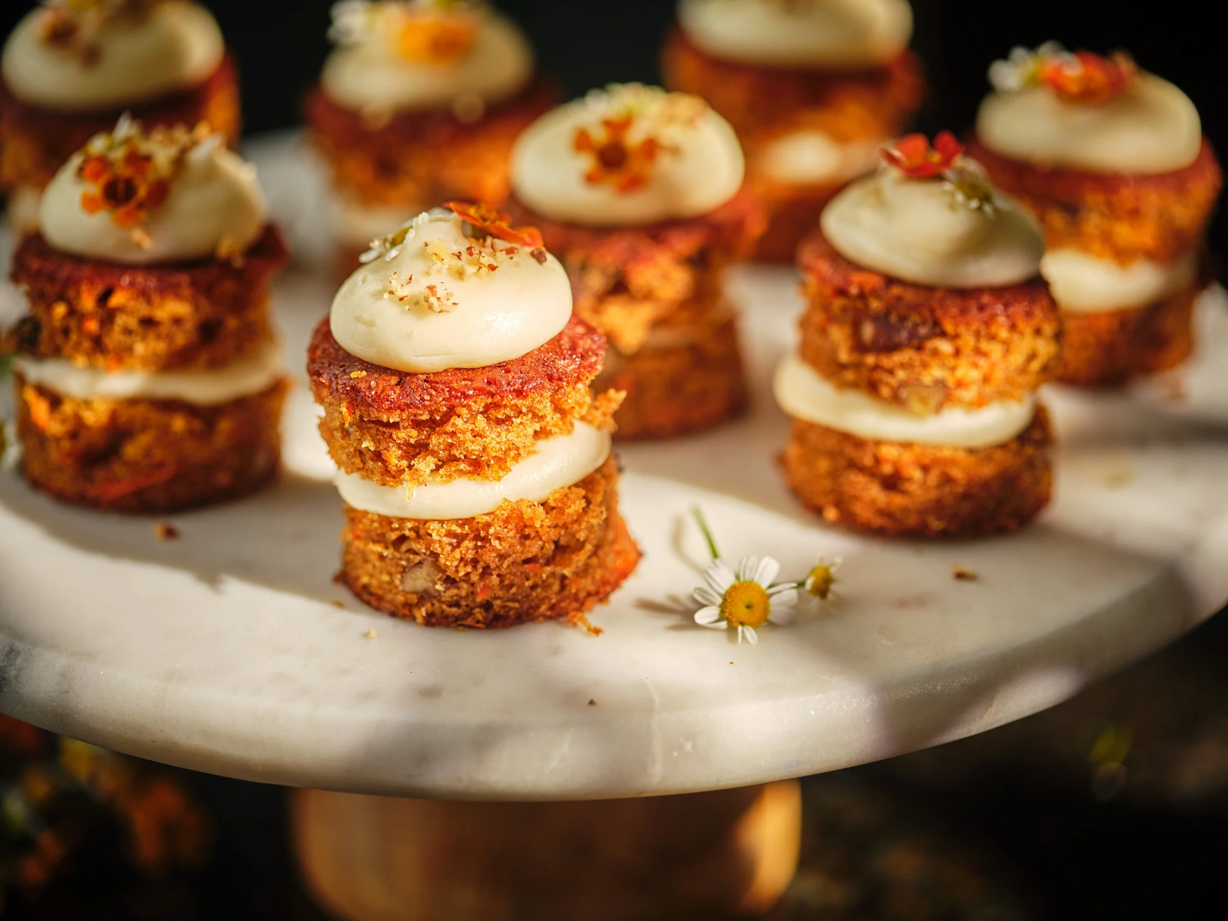Close-up of small layered desserts on a white plate, topped with cream, garnished with edible flowers and sprinkles.