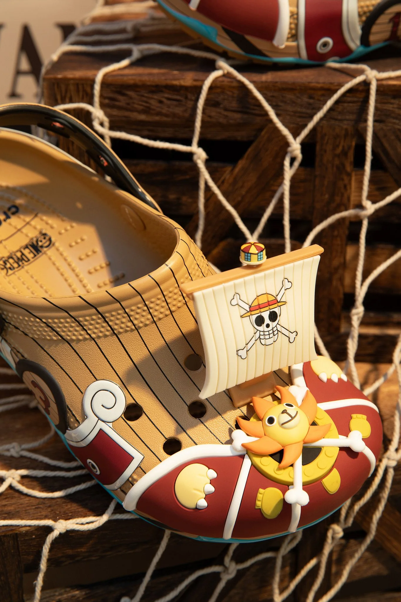 A colorful toy boat decorated with a cartoon pirate skull and crossbones, a small spinning ride with a yellow and orange lion figure, and a white bench with candy cane stripes, set on a wooden surface with a rope netting underneath.
