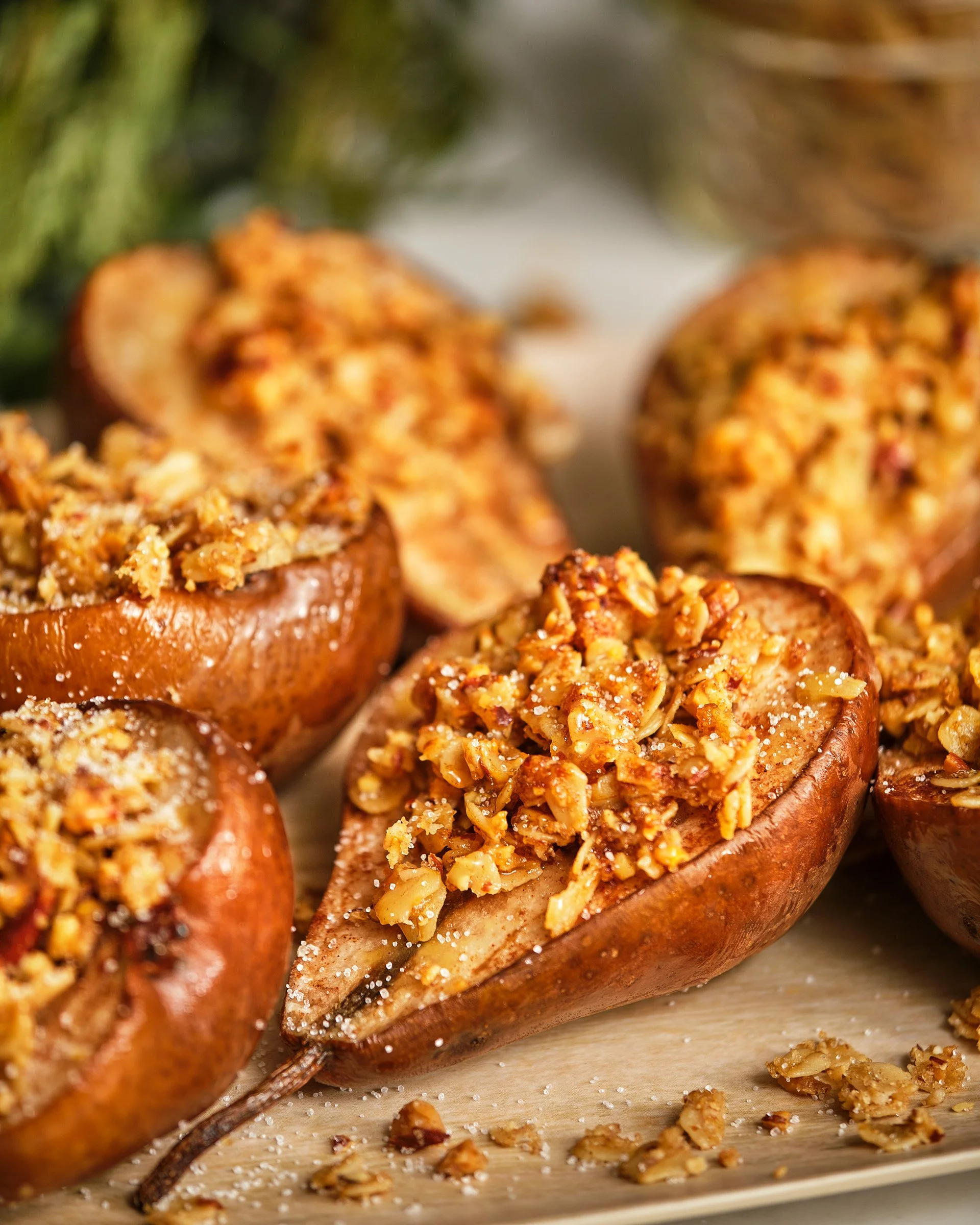 Close-up of halved baked apples stuffed with cinnamon-spiced granola, placed on a wooden surface with scattered granola pieces.