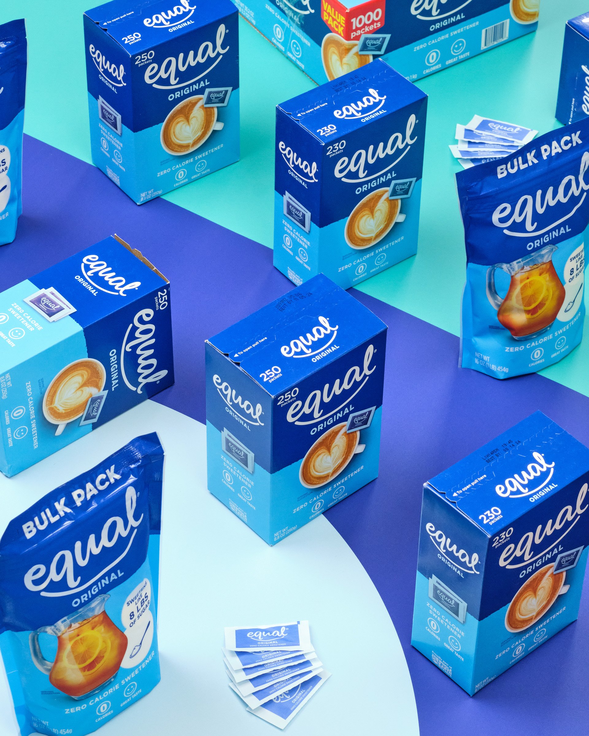 Various packs of Equal brand zero calorie sweetener, including boxes of individual packets and bulk packs, displayed on a colorful surface.