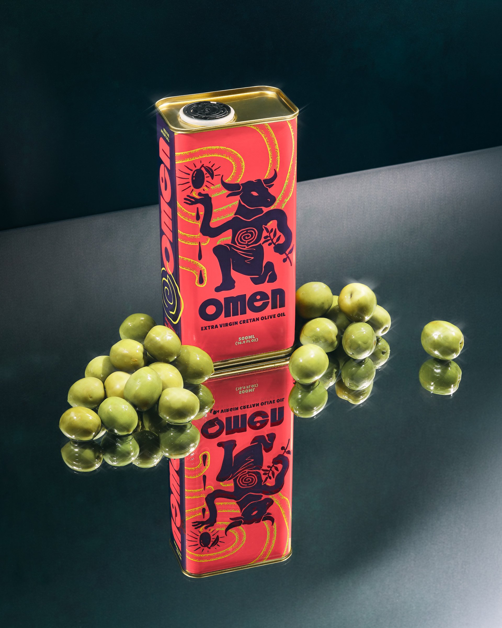 A rectangular tin container with a colorful design featuring a black bull with a spiral on its body, a black llama or alpaca, and a black sun with rays. The container is labeled "Olio" and contains extra virgin Cretan olive oil. It is placed on a dar