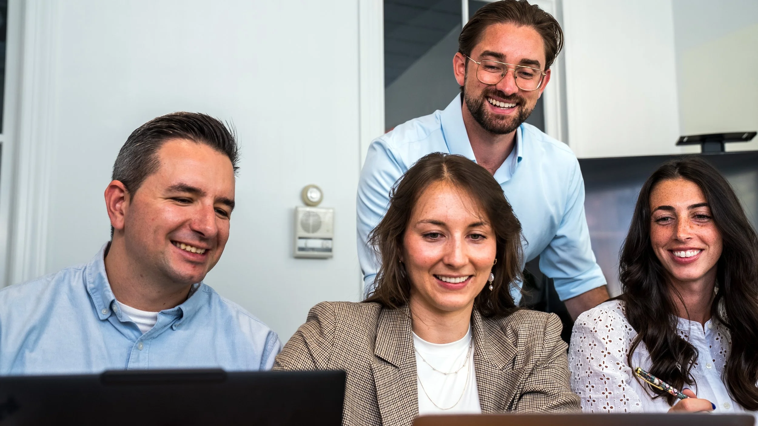 The Encora Therapeutics team gathered around a laptop, smiling and engaged in a collaborative work session in an office setting.