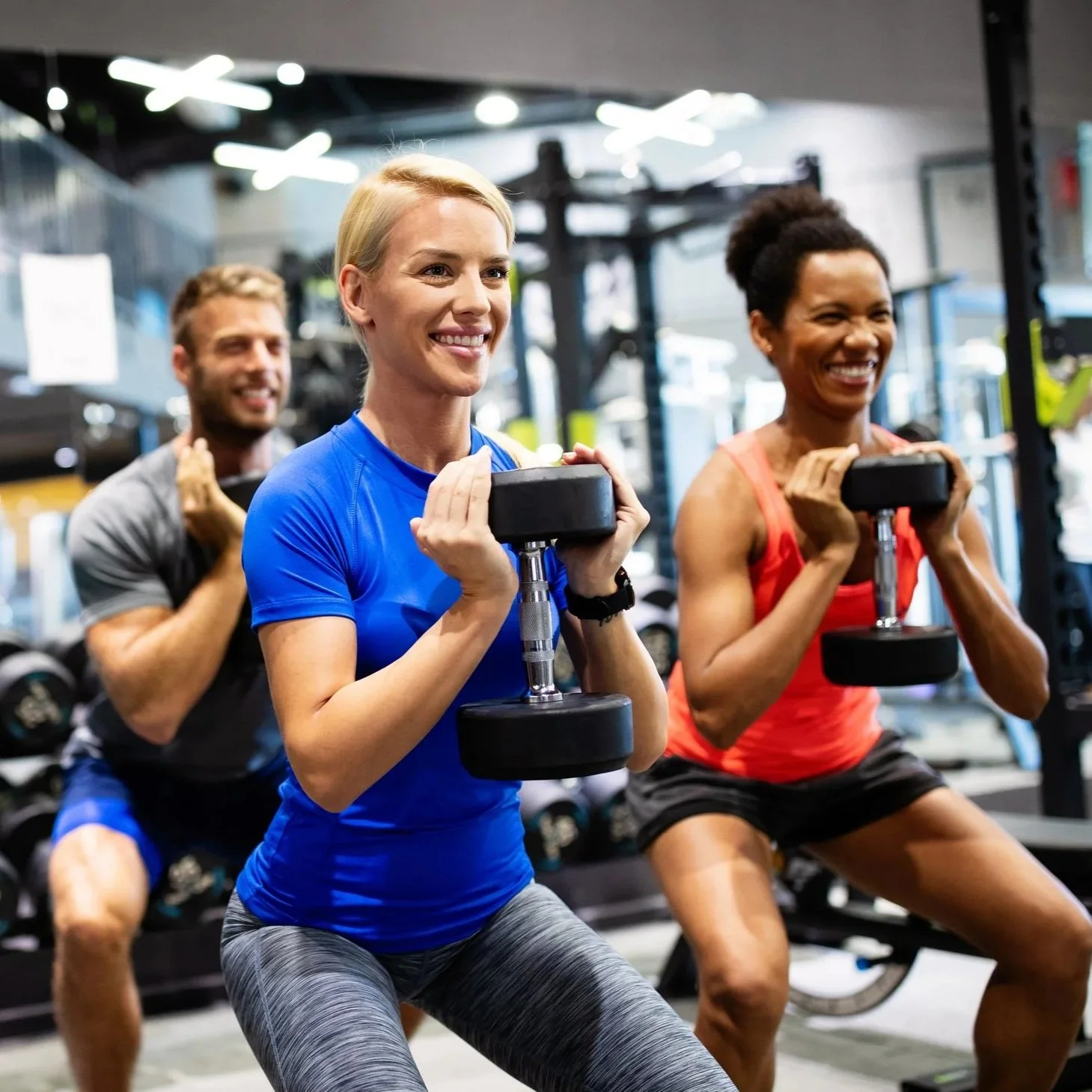 Three people working out with dumbbells in a gym, smiling and lifting weights.