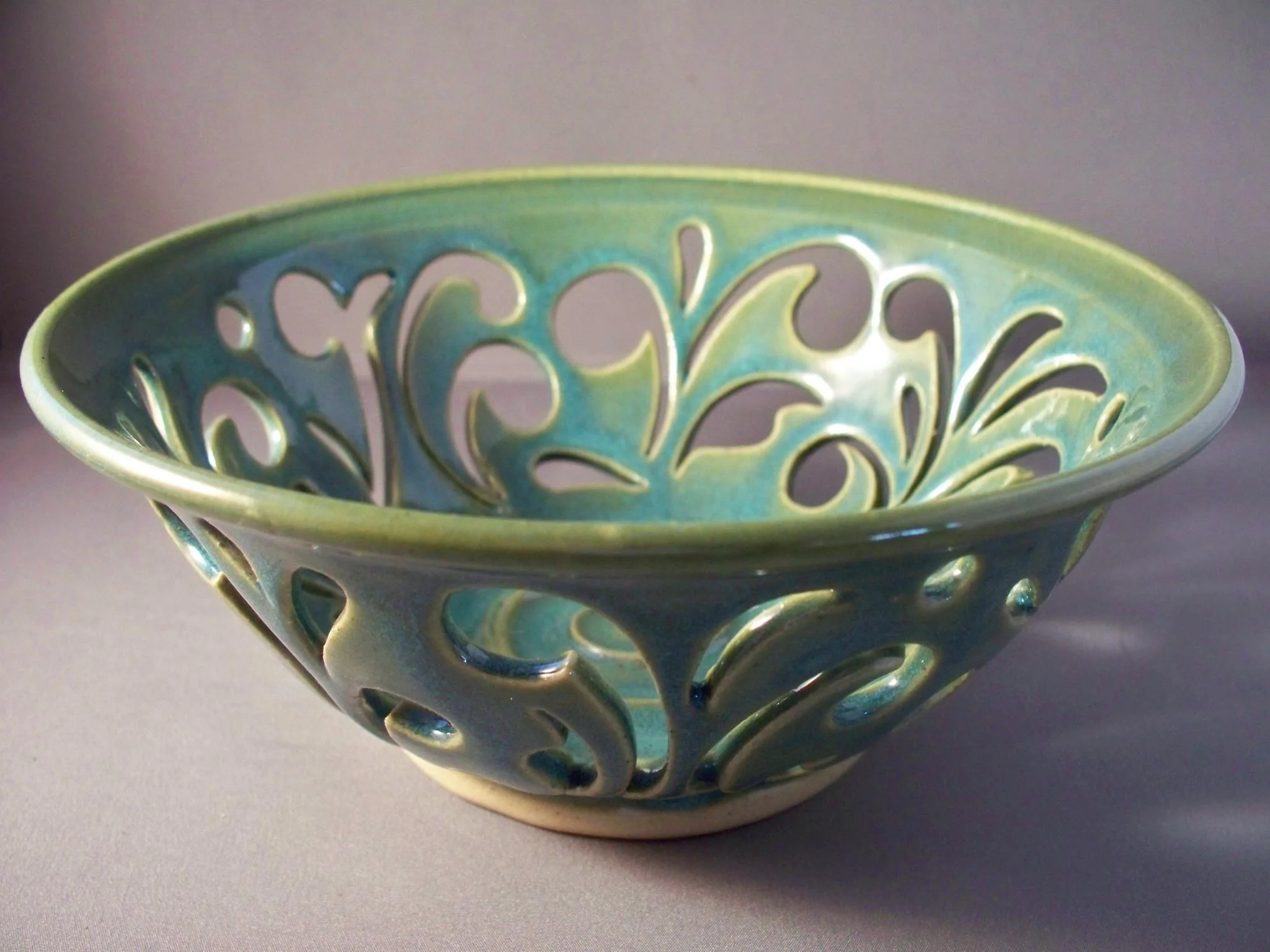 A ceramic bowl with a floral or vine pattern, glazed in shades of blue and green, with an openwork design around the rim and base