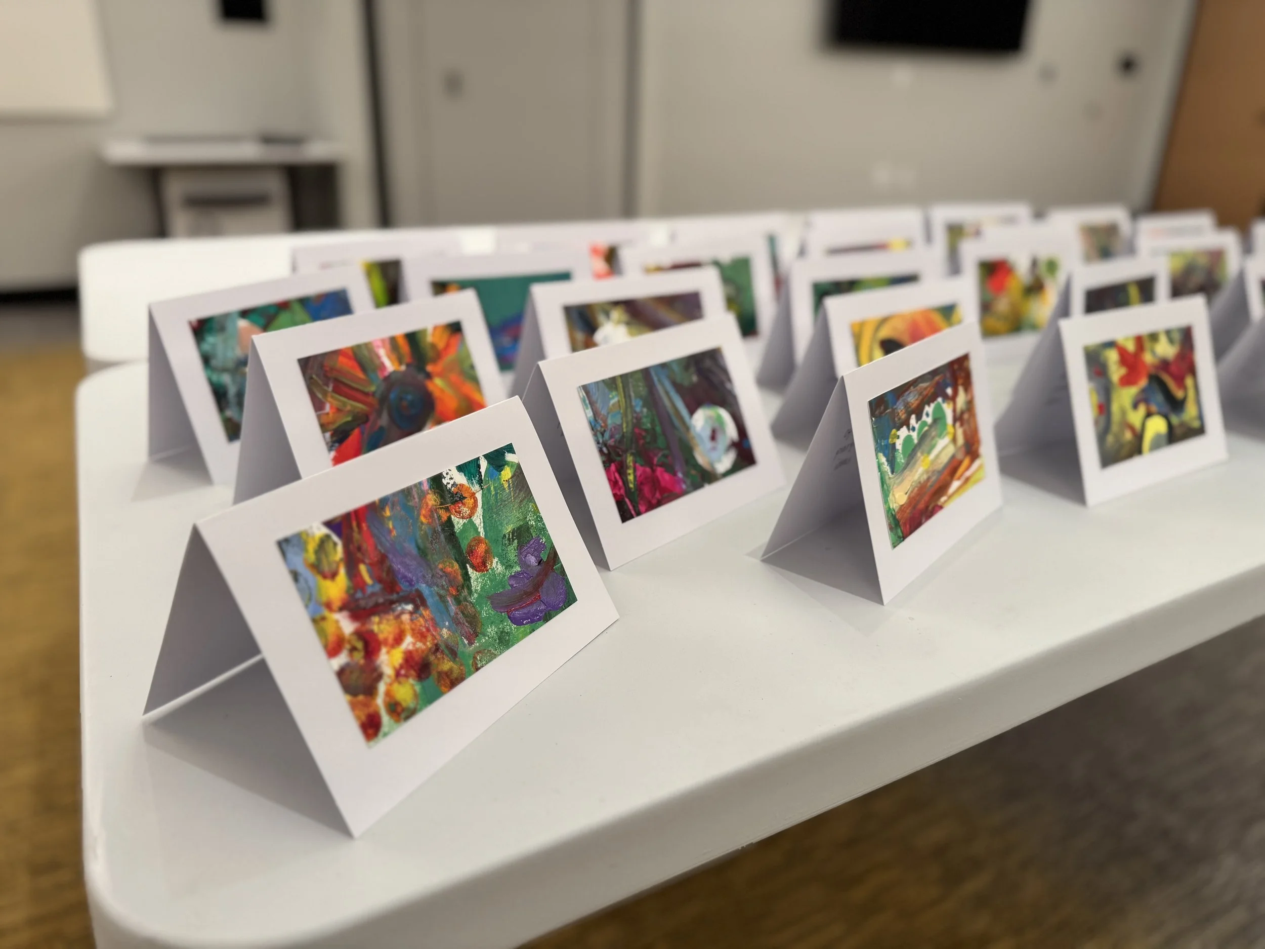 Colorful abstract artwork displayed on small greeting cards arranged on a white table.