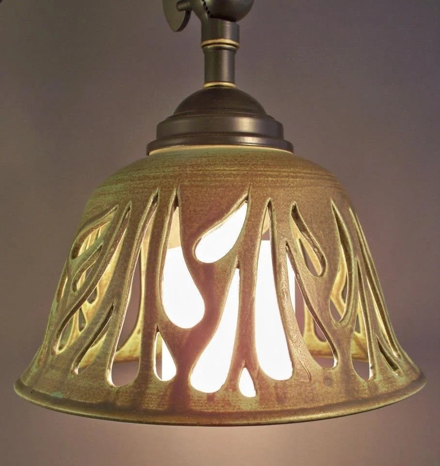 A ceiling light fixture with a beige, cut-out metal lampshade design and a metal dome on top, turned on and illuminating.