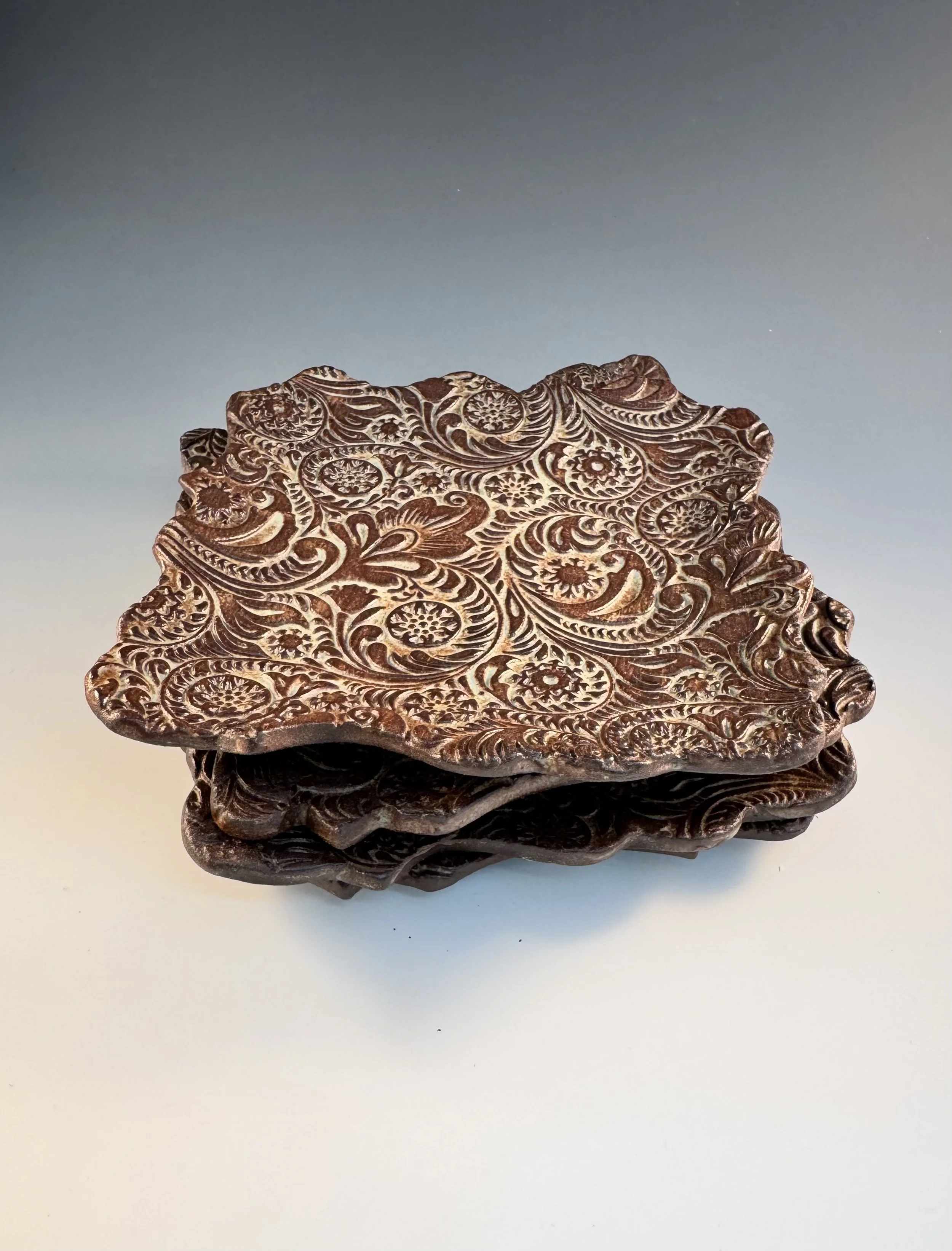 Close-up of an ornate, carved wooden box with swirling patterns, reflecting on a white surface against a gradient sky background.