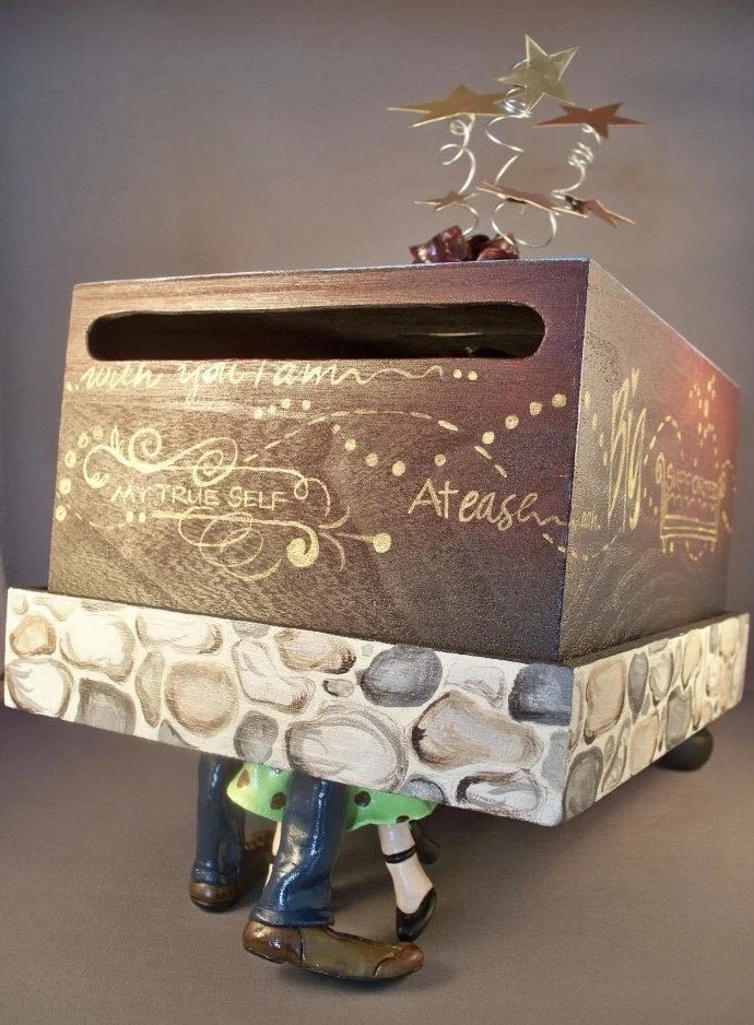 A decorative tissue box holder designed as a horse, with the tissue box on its back. The tissue box is brown with gold writing and a stone pattern on the sides, resting on the horse's legs and hooves.