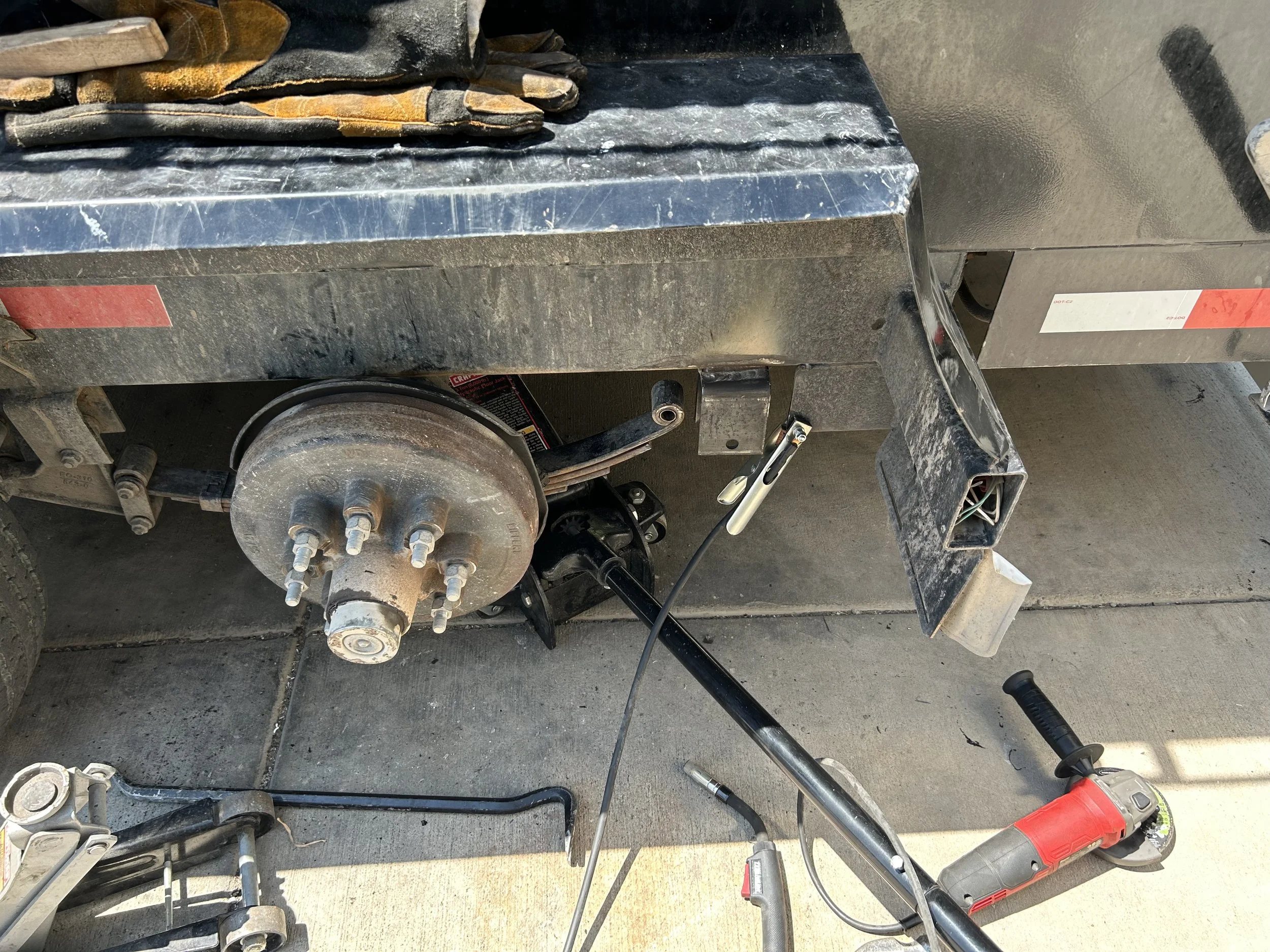 Close-up of a metal work surface with tools and equipment around, including a cordless drill, wrenches, and a piece of machinery or metal part with bolts and electrical wiring.
