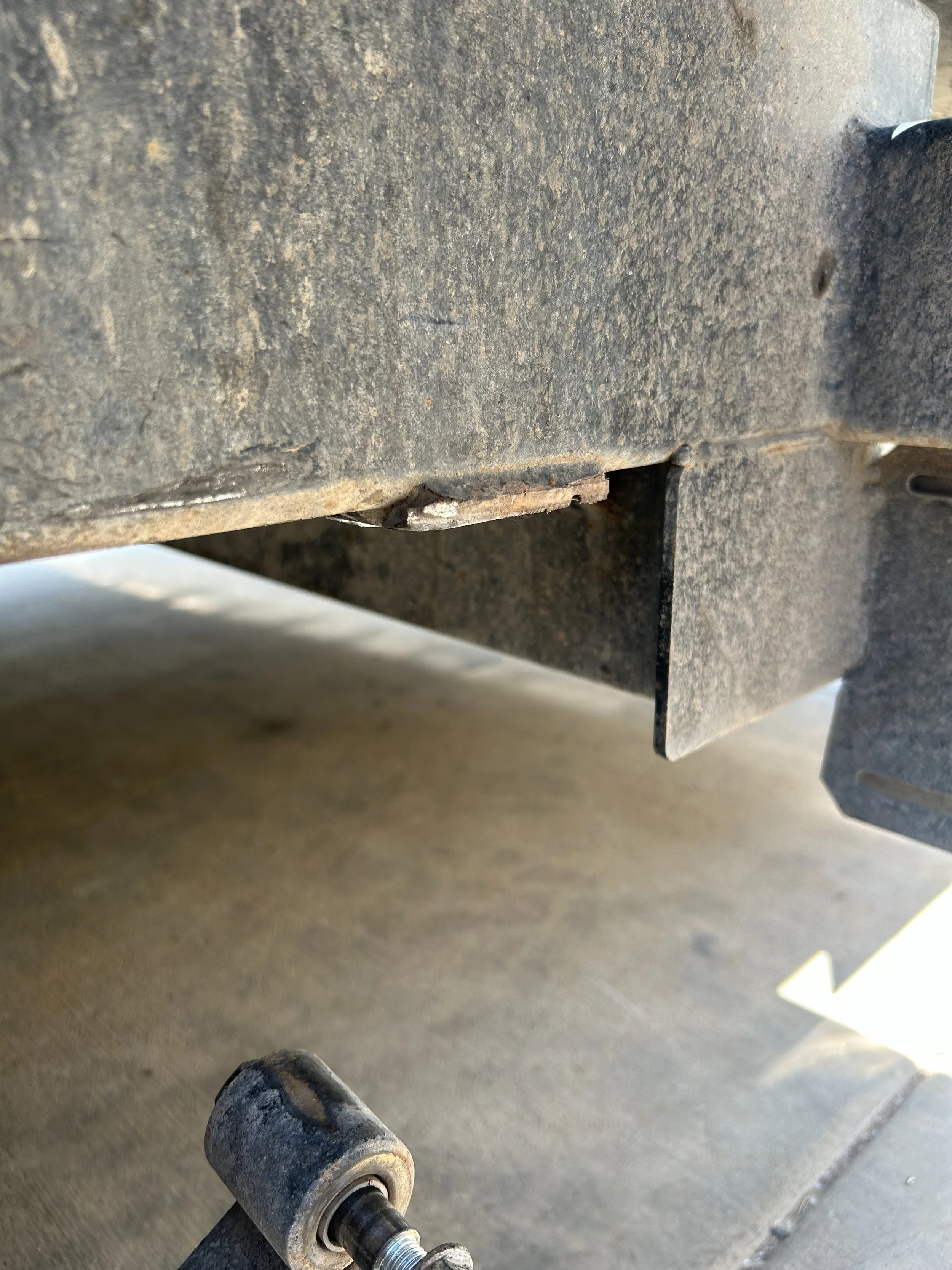 Close-up of a rusty metal machinery part, possibly a roller or wheel, on a dirt or worksite floor.