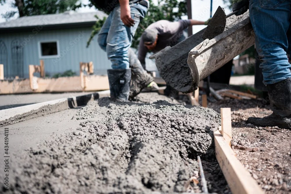 Construction workers pouring and leveling concrete on a sidewalk or driveway.