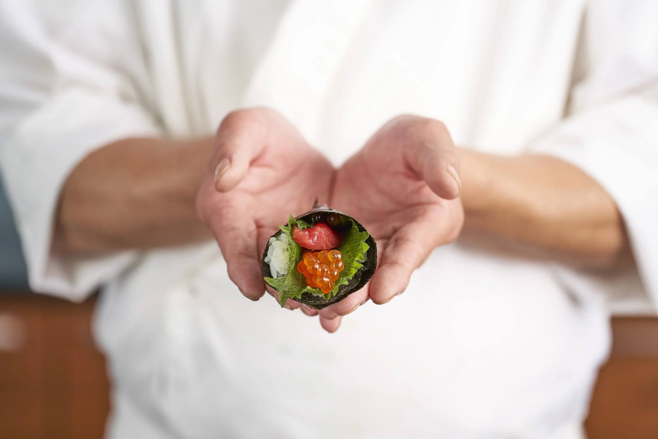 Person holding a sushi roll with visible ingredients including rice, fish roe, lettuce, and fish.