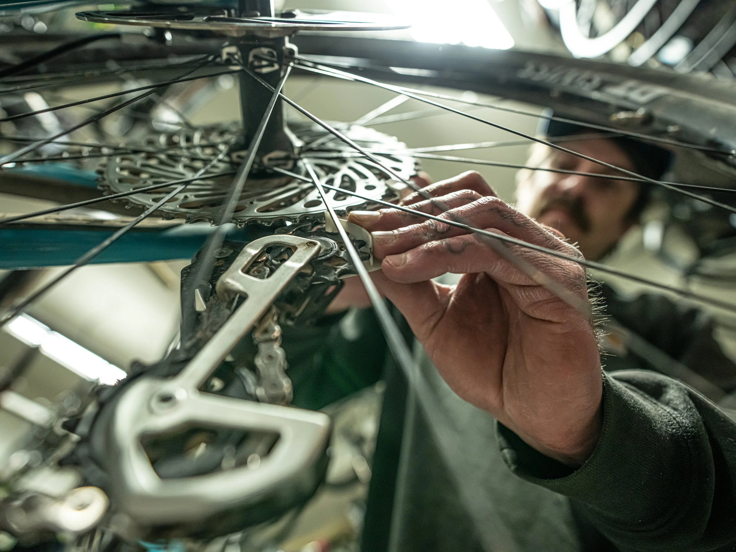 Close-up of a person repairing a bicycle, focusing on hands working on the bike's hub and gears, with spokes and gear cassette visible.