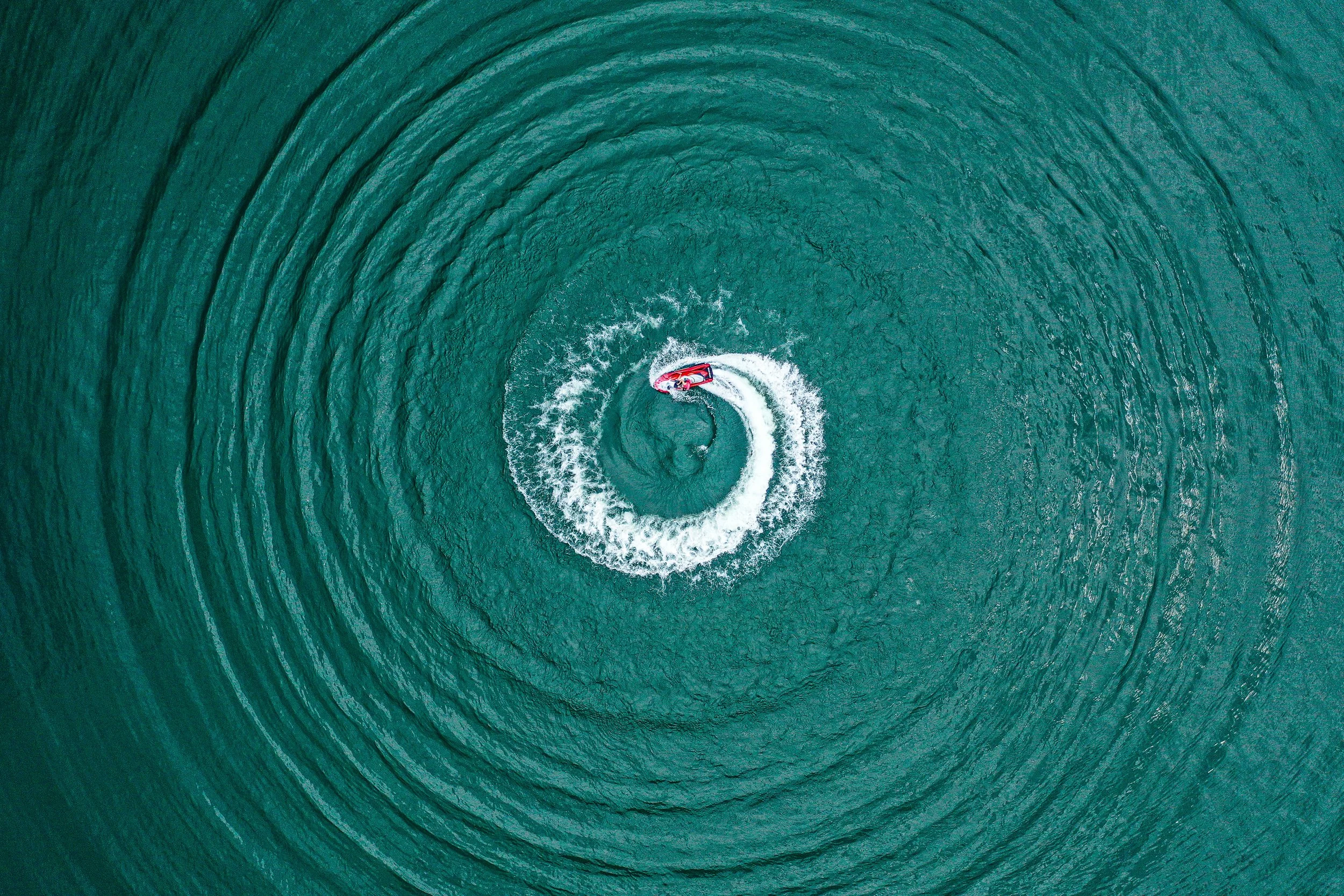 Aerial view of a person wakeboarding on a large body of water, creating circular ripples.